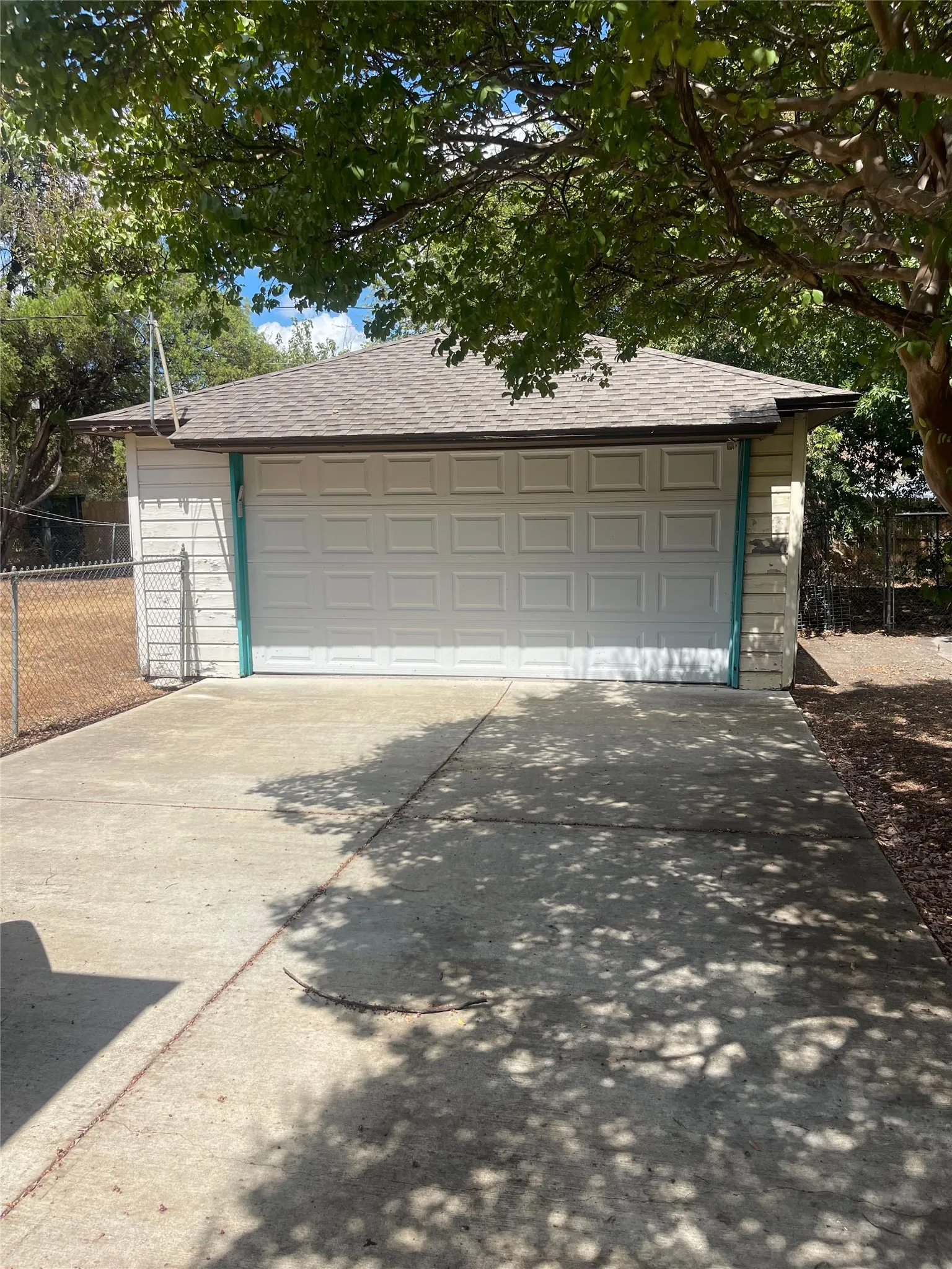 Detached garage with a paneled door, pitched roof, and concrete driveway