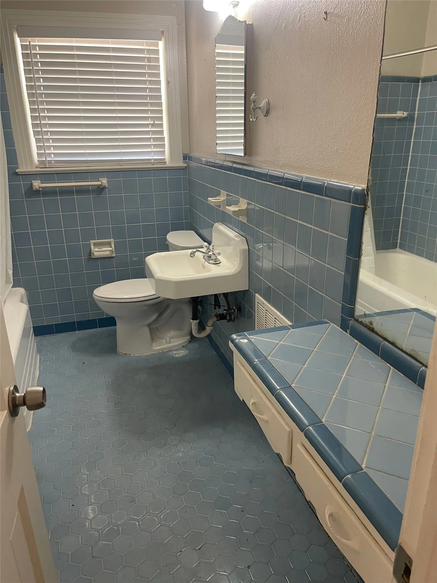 Bathroom featuring light blue tiled walls, hexagonal floor tiling, a white wall-mounted sink, and a built-in storage bench with tiled top