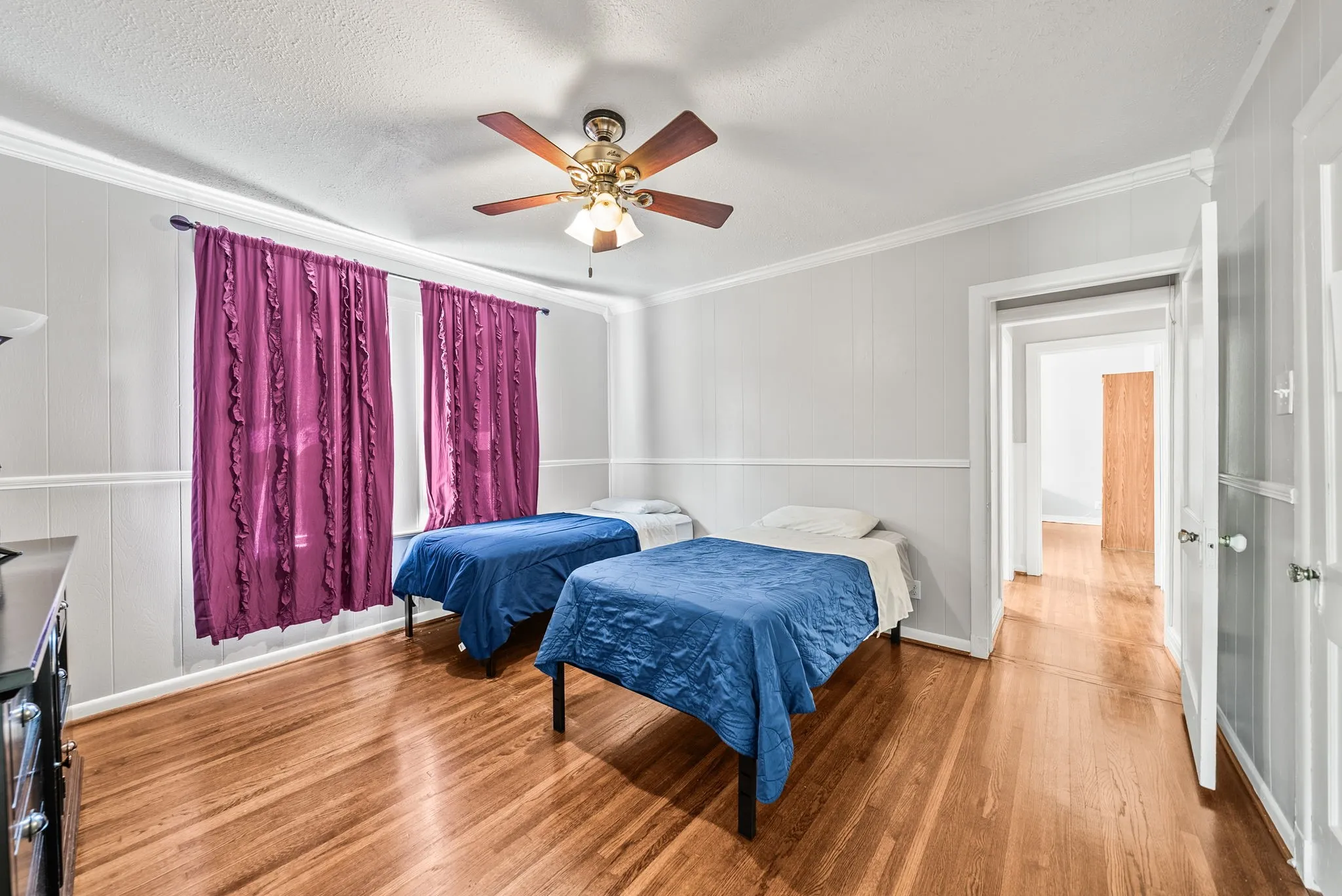 Hardwood flooring with a warm finish, wall paneling, crown molding, and a ceiling fan with integrated lighting