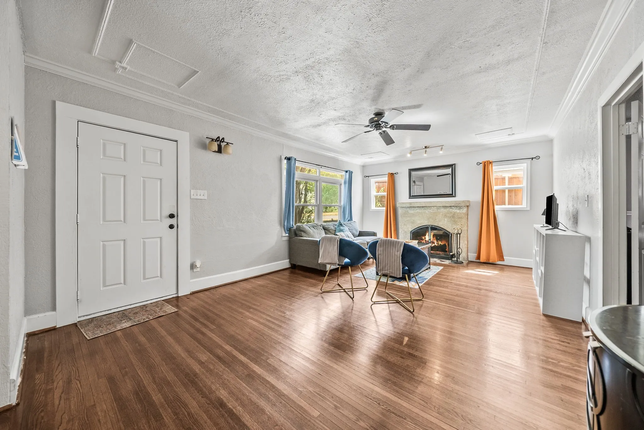 Wood-finish flooring throughout, a ceiling fan, a stone-faced fireplace, crown molding, and multiple windows