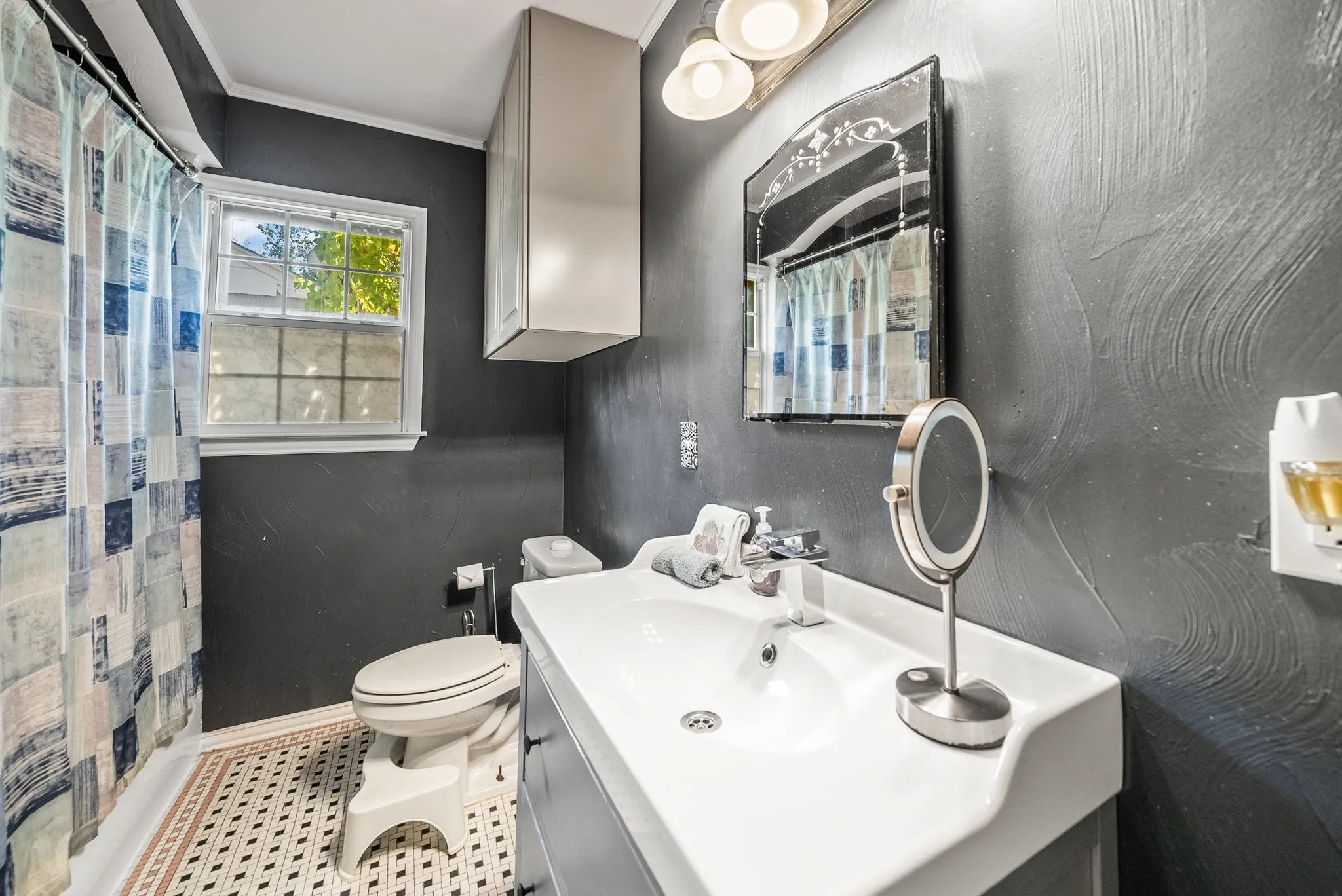 Bathroom featuring a single vanity with integrated sink, wall-mounted cabinetry, a window with privacy glass, and patterned floor tiling
