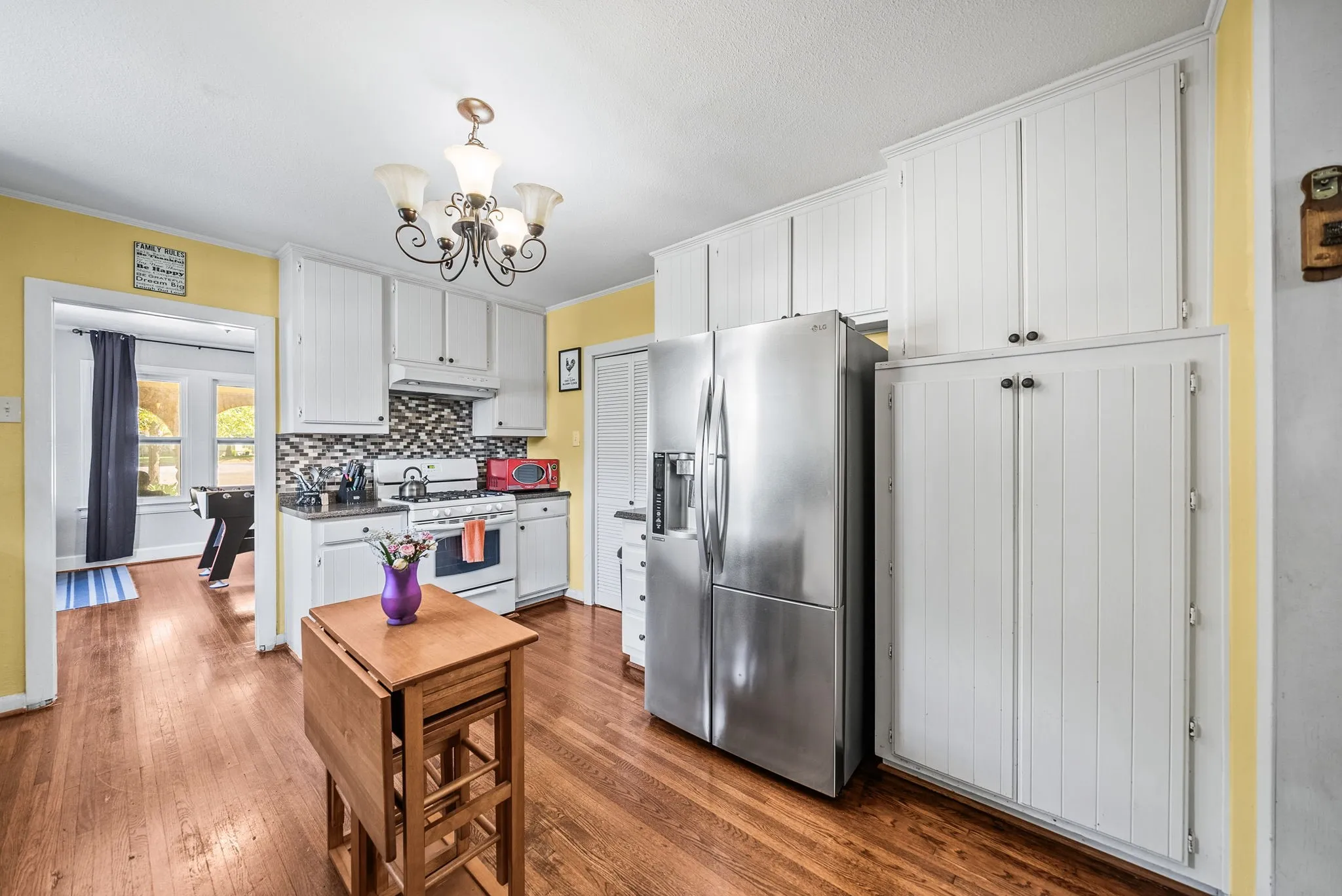 Kitchen featuring wood-finish flooring, white cabinetry, a mosaic tile backsplash, and a stainless steel refrigerator