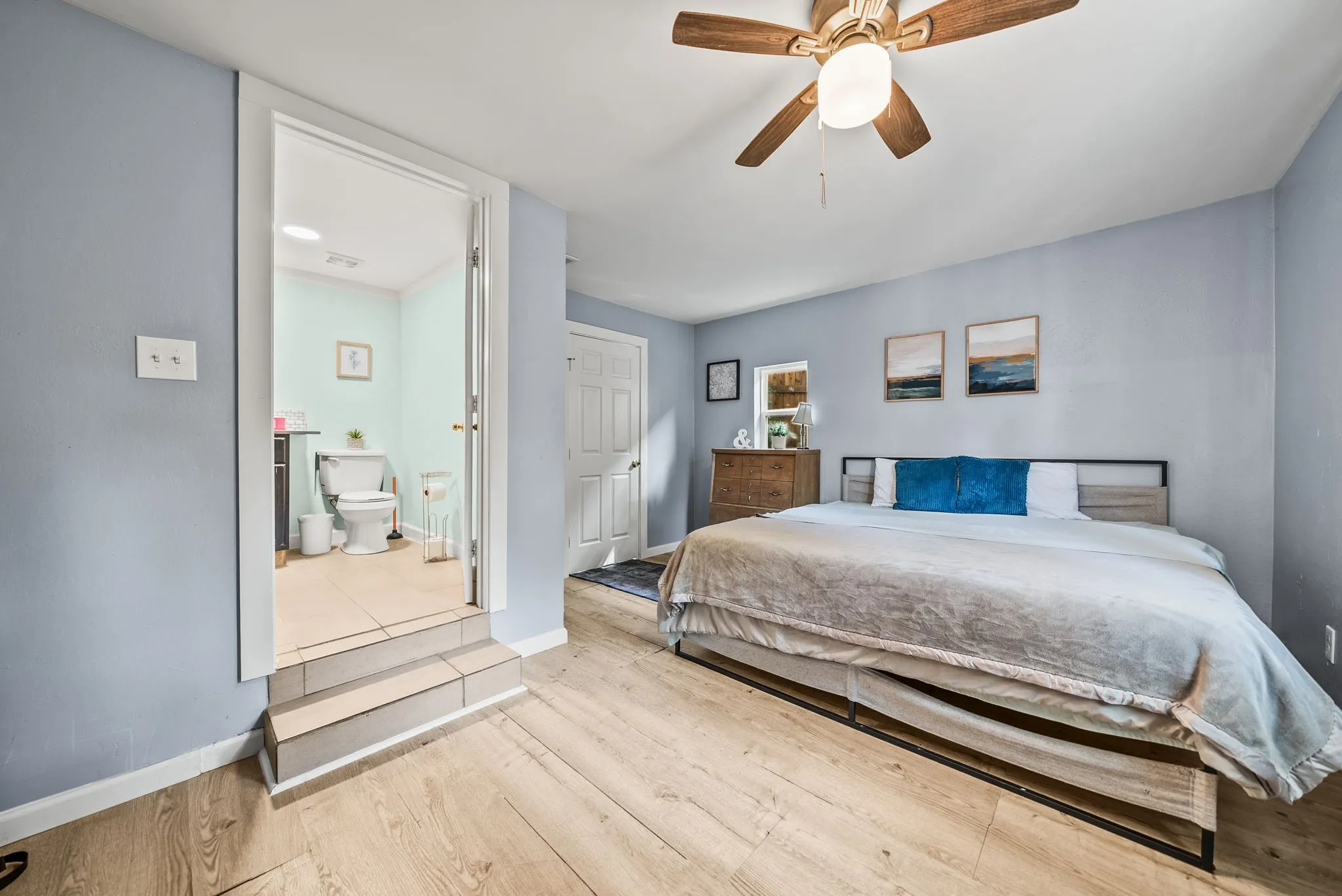 Wood-finish flooring throughout, ceiling fan with integrated lighting, and a private attached bathroom featuring tile flooring