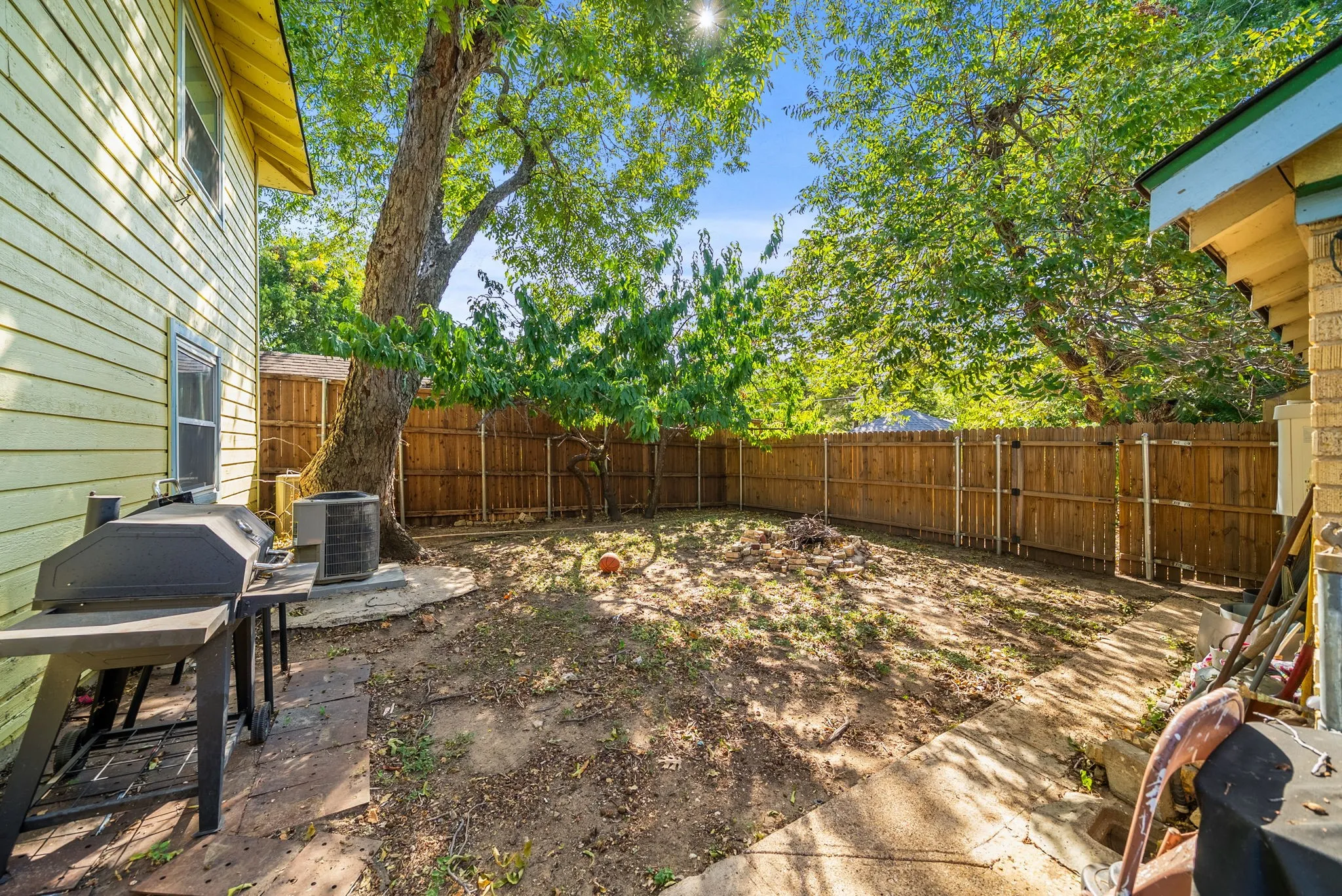 Expansive backyard featuring a wood fence, mature trees, and a concrete patio