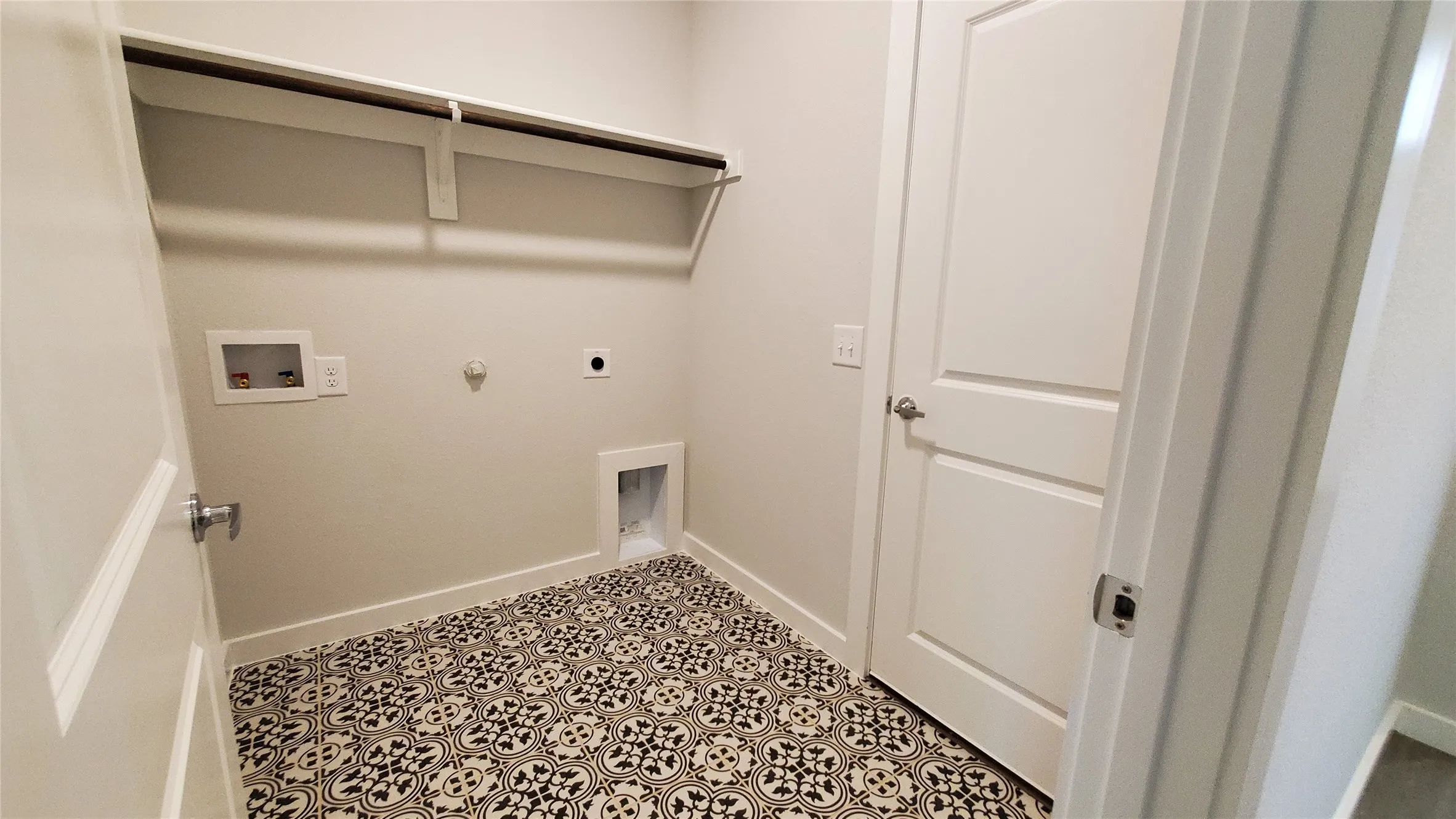 Laundry area with patterned floor tile, overhead shelving, and a hanging rod