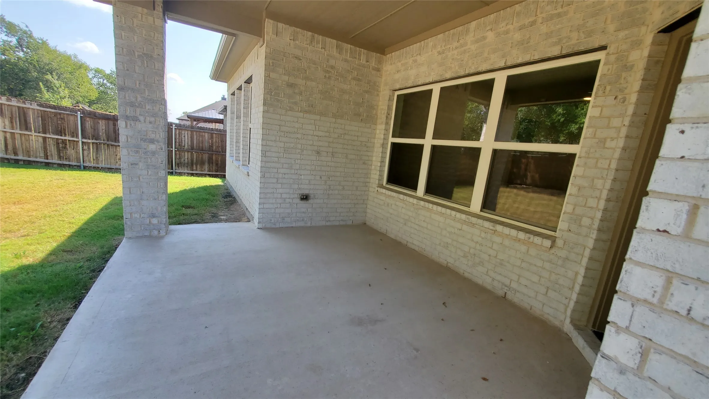 Covered patio featuring a concrete surface, light brick exterior, and a manicured lawn