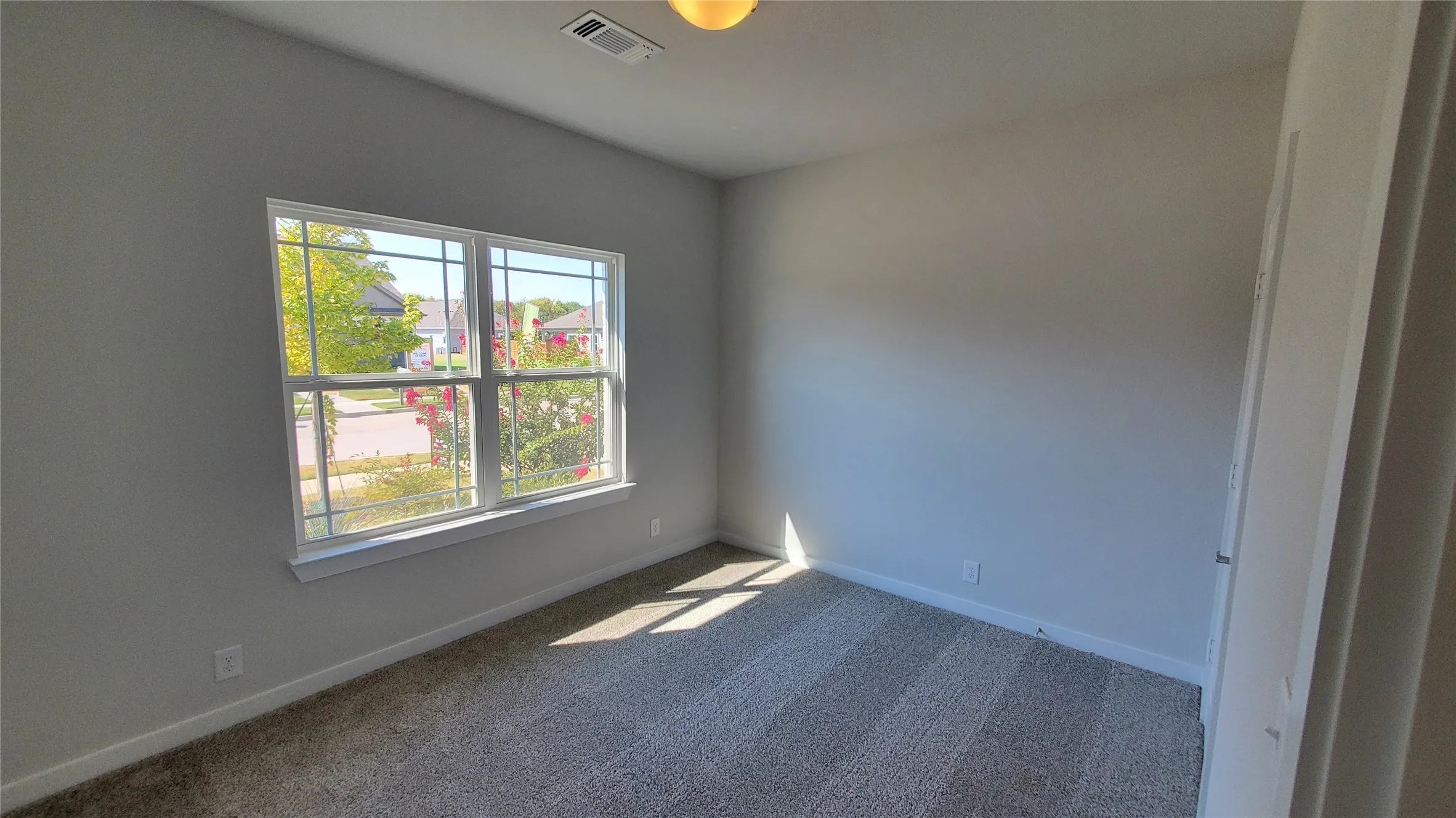 Neutral tone wall paint, light-colored carpet, ceiling-mounted light fixture, white trim, and a window with white sashes