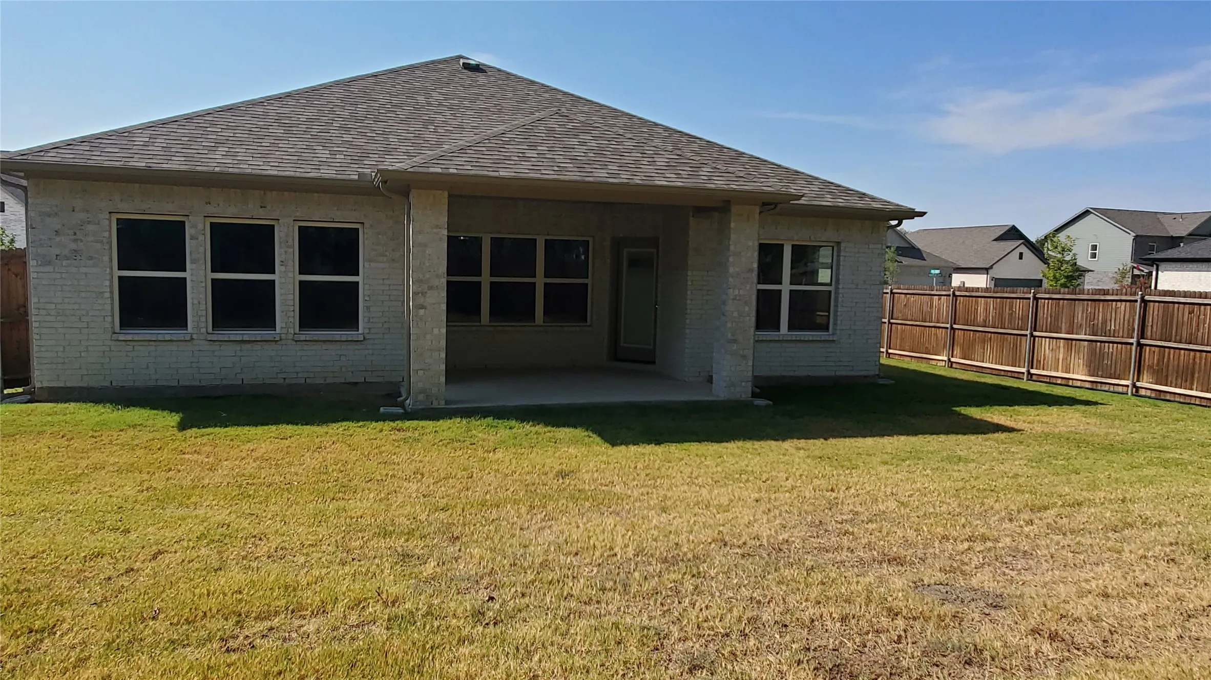 Expansive backyard with a covered patio, privacy fencing, and a full brick exterior