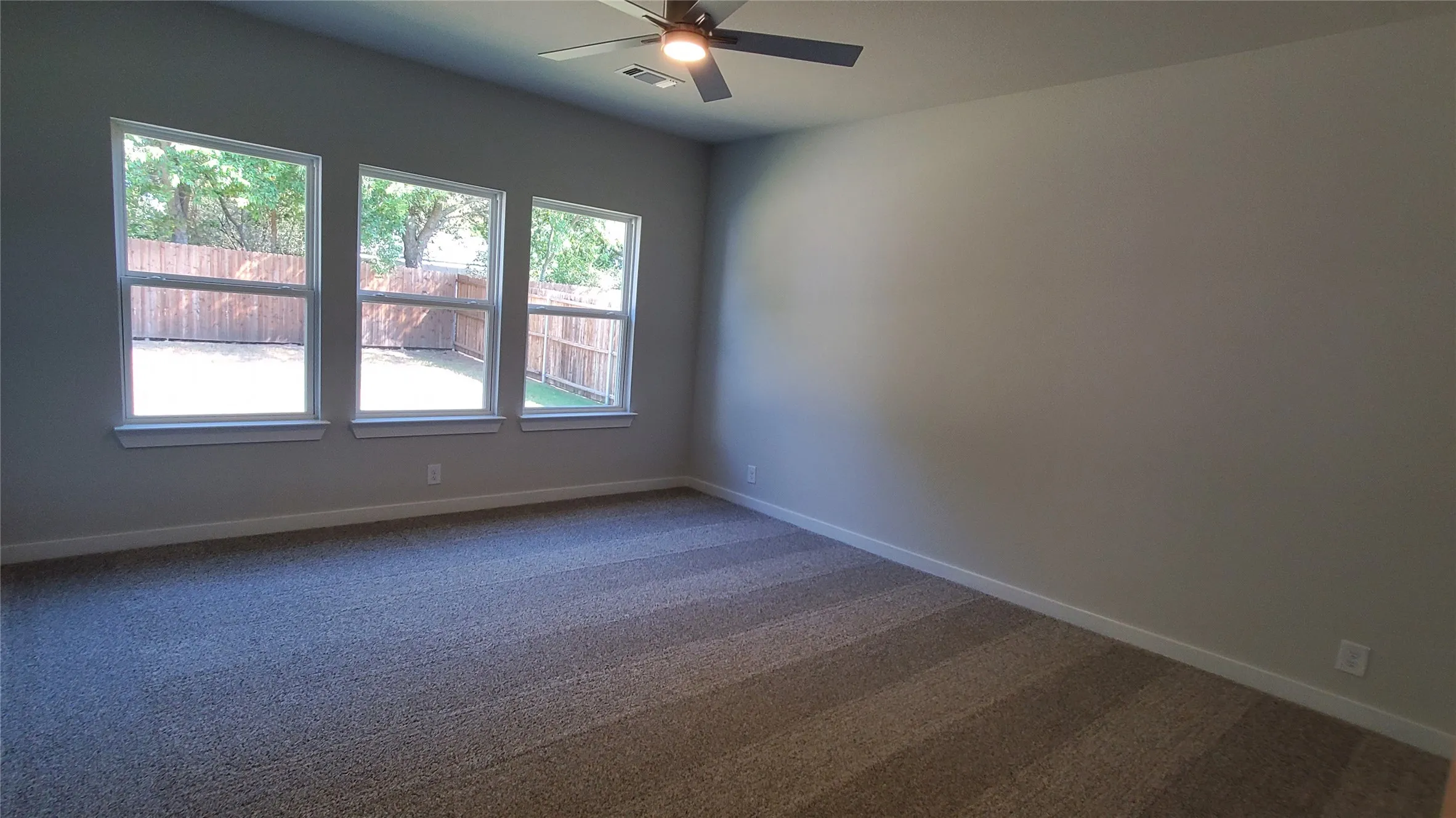 Vaulted ceiling with a ceiling fan, three large windows, textured walls, and carpet flooring
