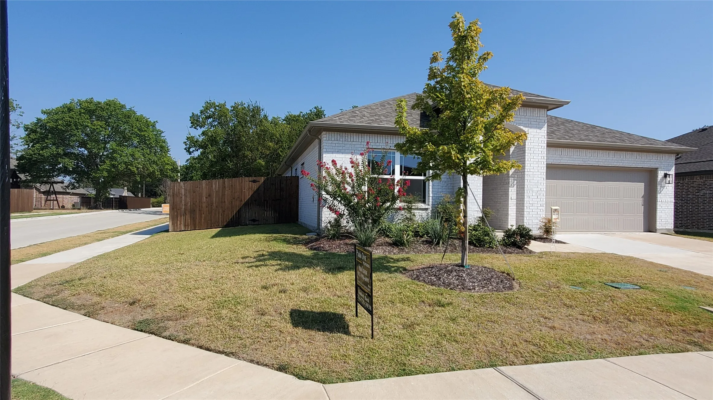 White brick exterior with a gray garage door, concrete driveway, and a wood privacy fence
