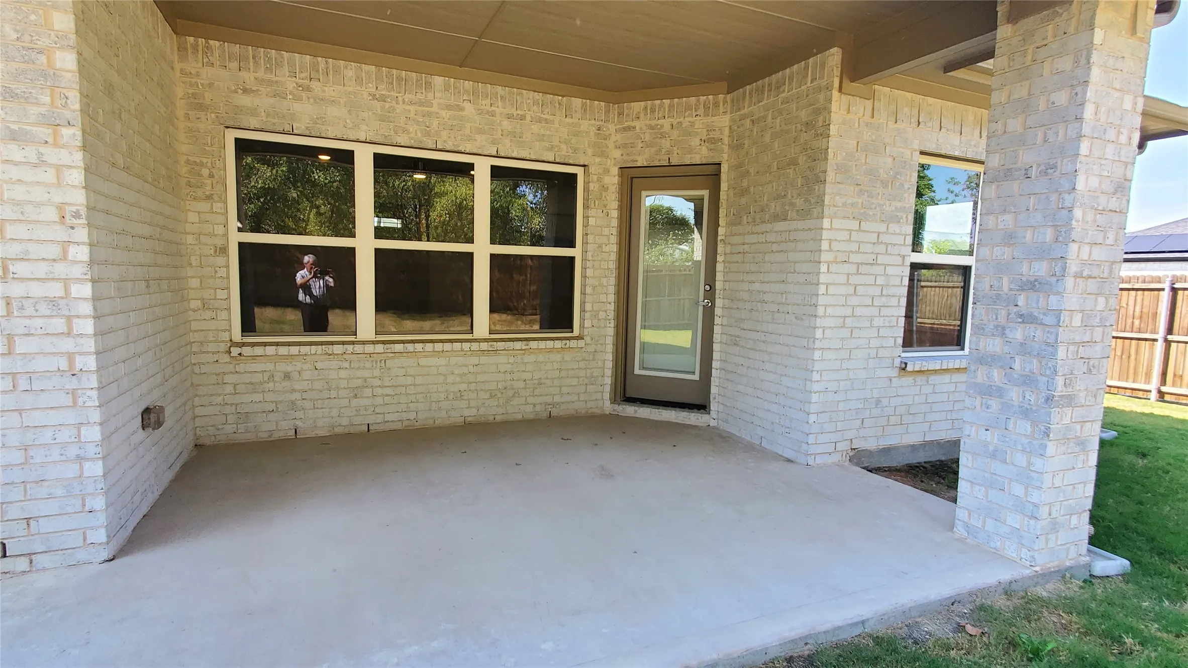 Covered patio with concrete flooring, light-toned brick exterior, and a glass-paneled door