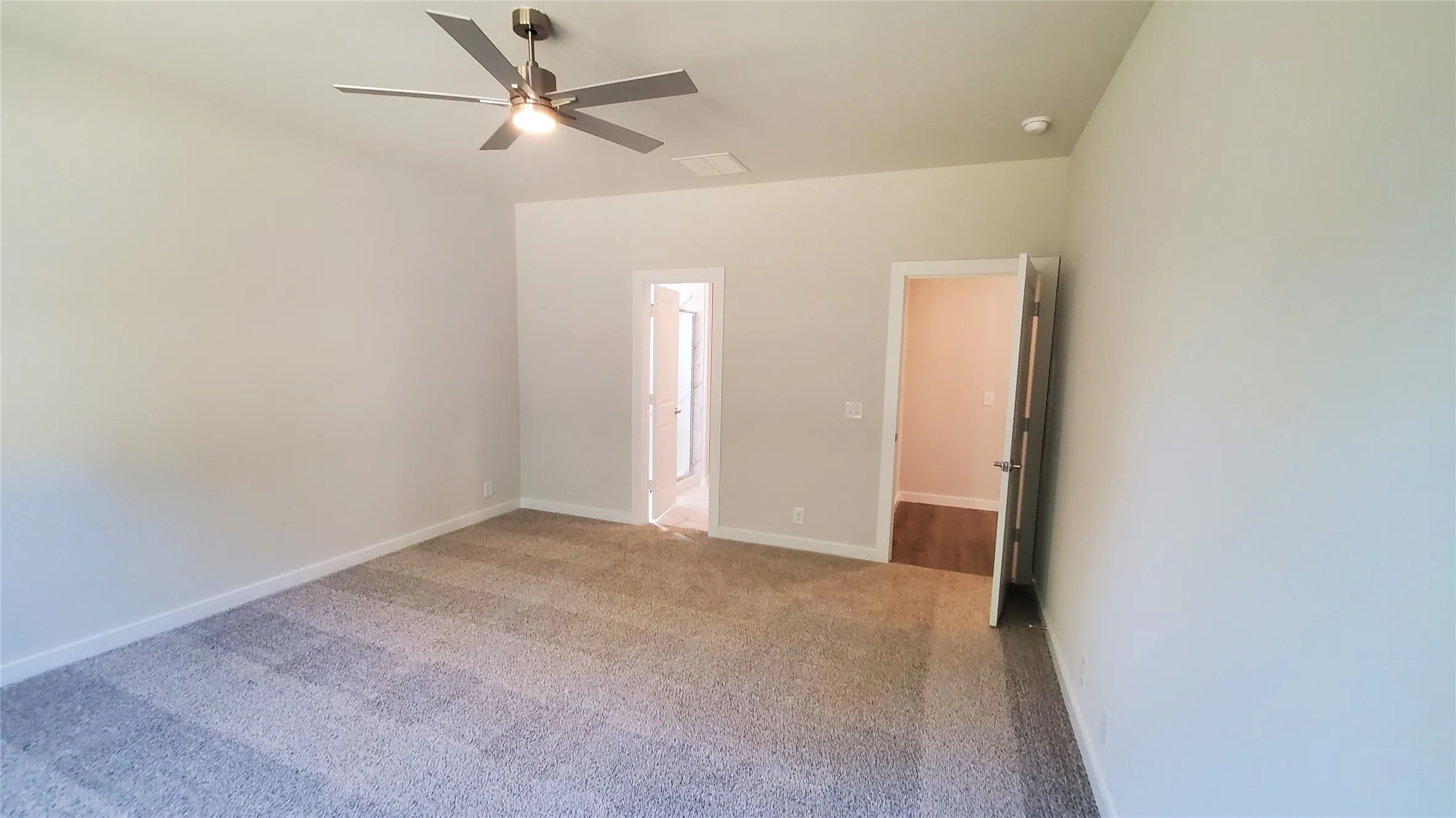 Neutral tone wall finishes, gray textured carpet, and a contemporary ceiling fan with integrated lighting