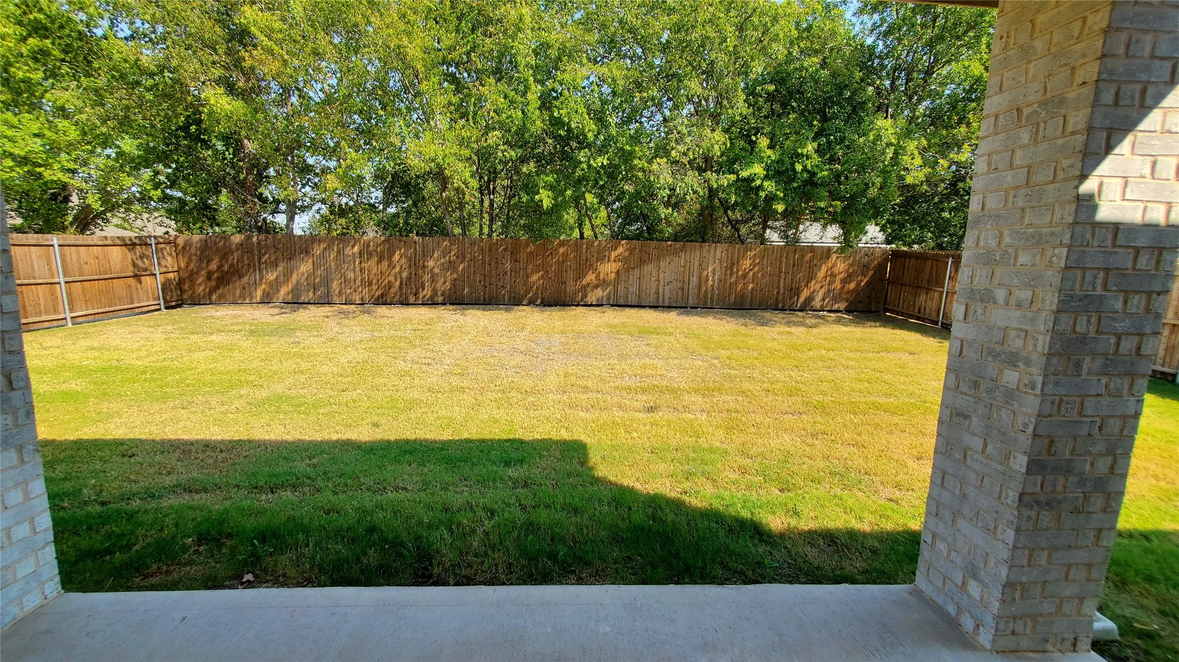 Expansive backyard featuring a privacy fence, mature trees, and a concrete patio