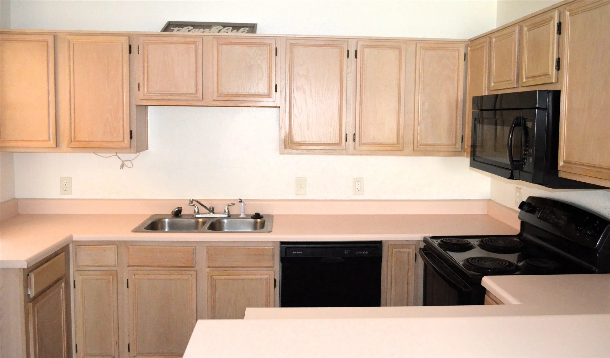 U-shaped kitchen featuring wood-finish cabinetry, a double basin stainless steel sink, black electric range, black microwave, and black dishwasher