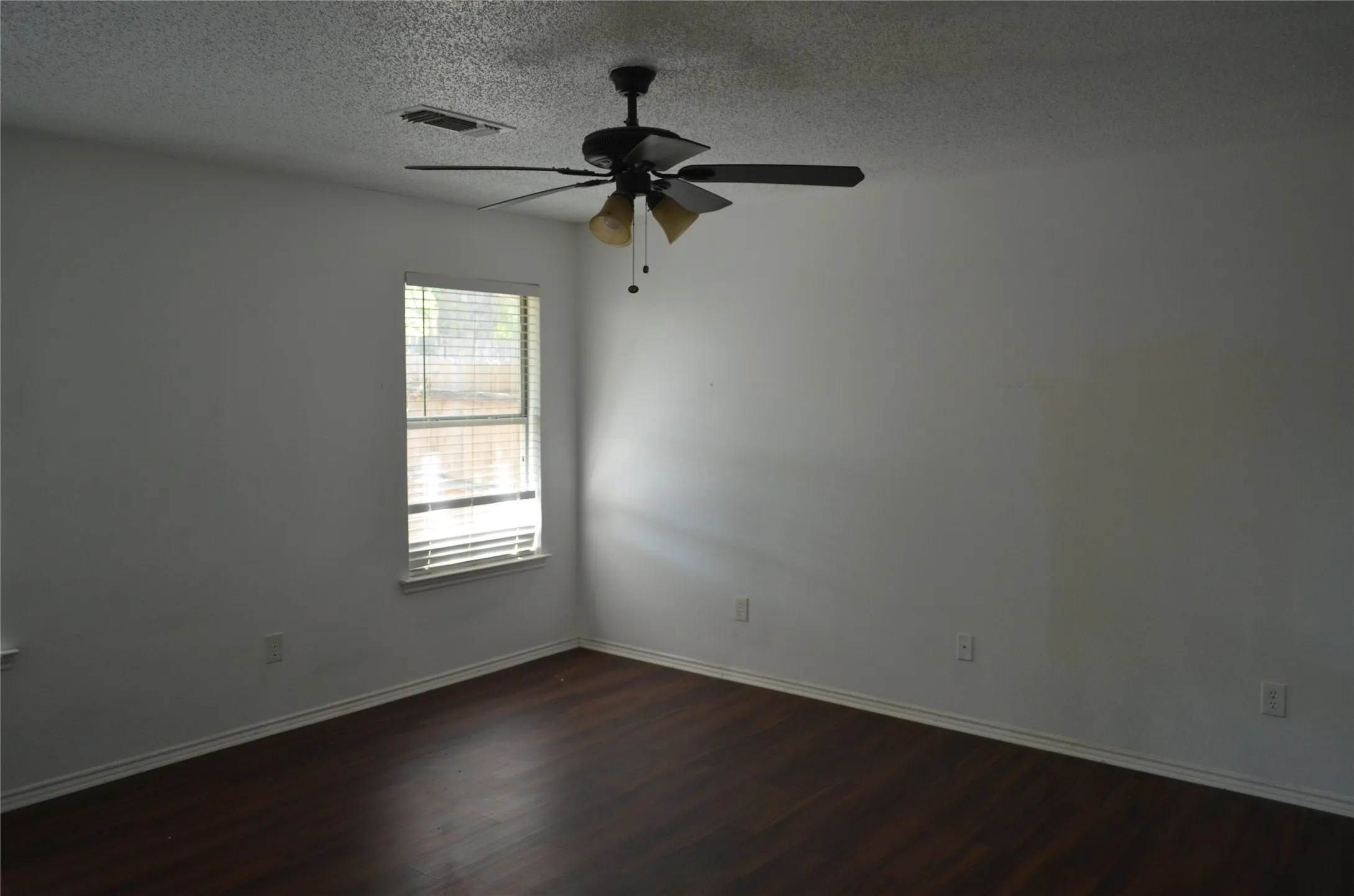 Wood-finish flooring with white walls, a single window with blinds, and a ceiling fan with integrated lighting