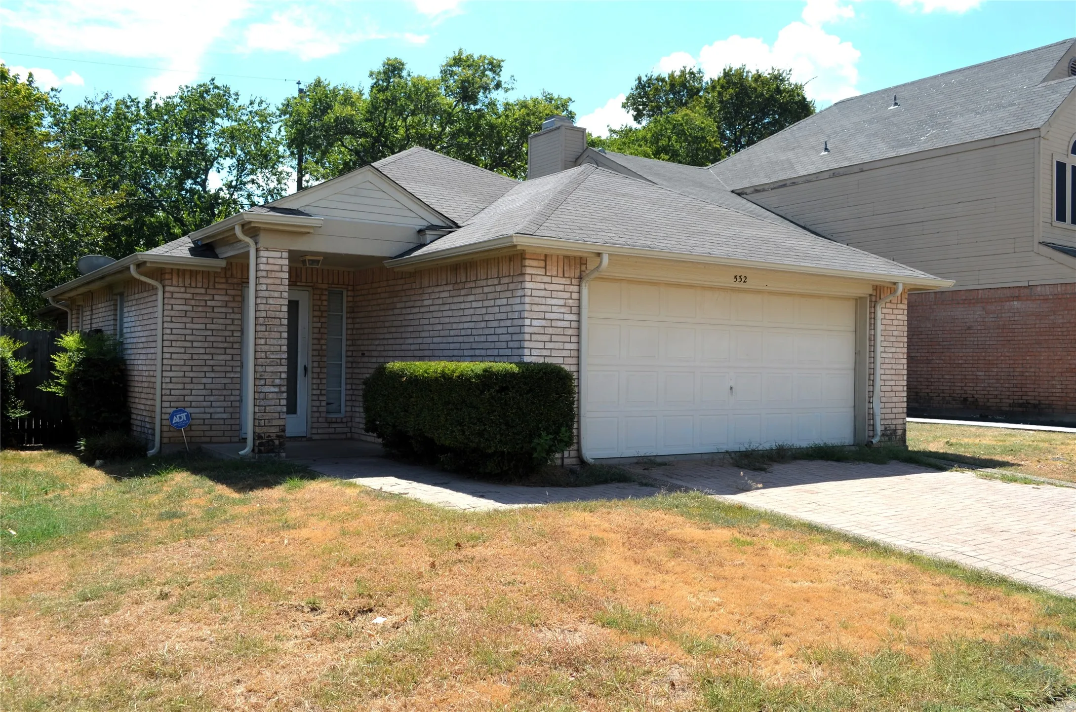 Brick exterior with an attached garage, paved driveway, and covered entryway