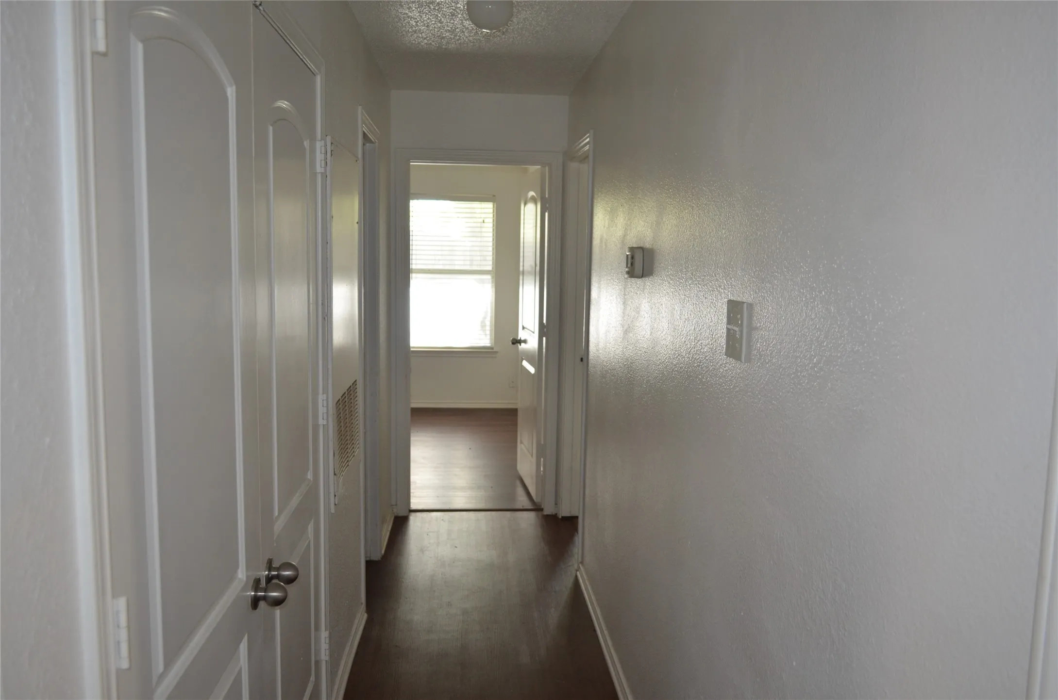 White interior walls, wood-finish flooring, white paneled doors, and a ceiling-mounted light fixture
