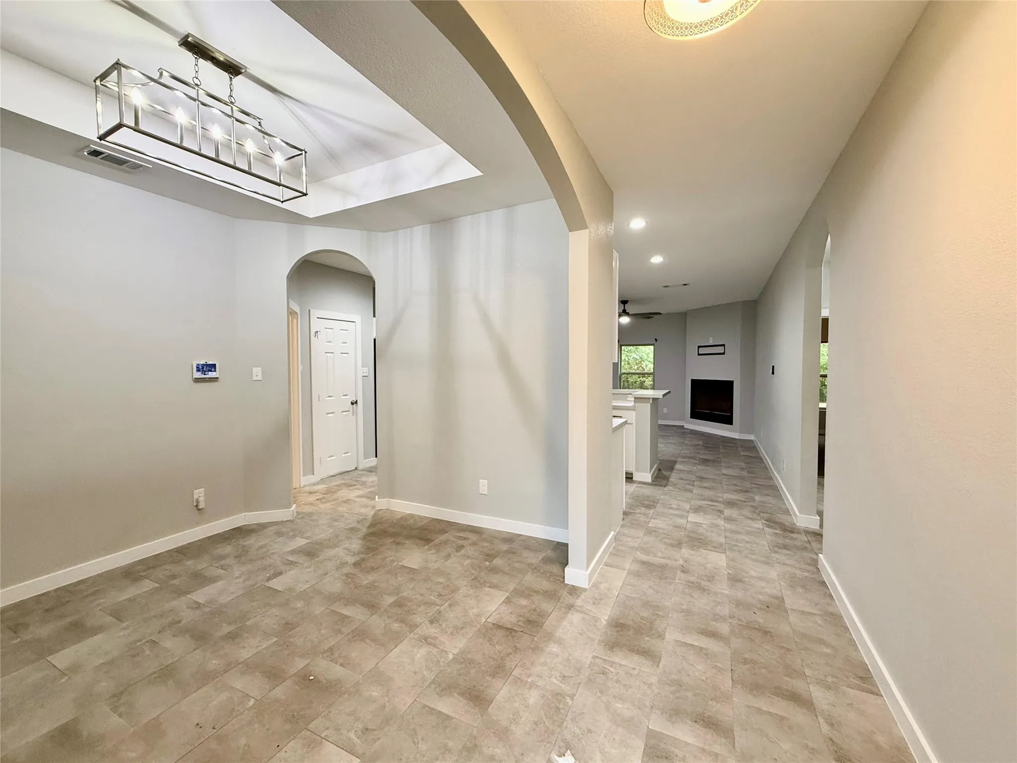 Recessed ceilings with modern rectangular chandelier, neutral wall paint, arched doorways, tile flooring, and built-in fireplace