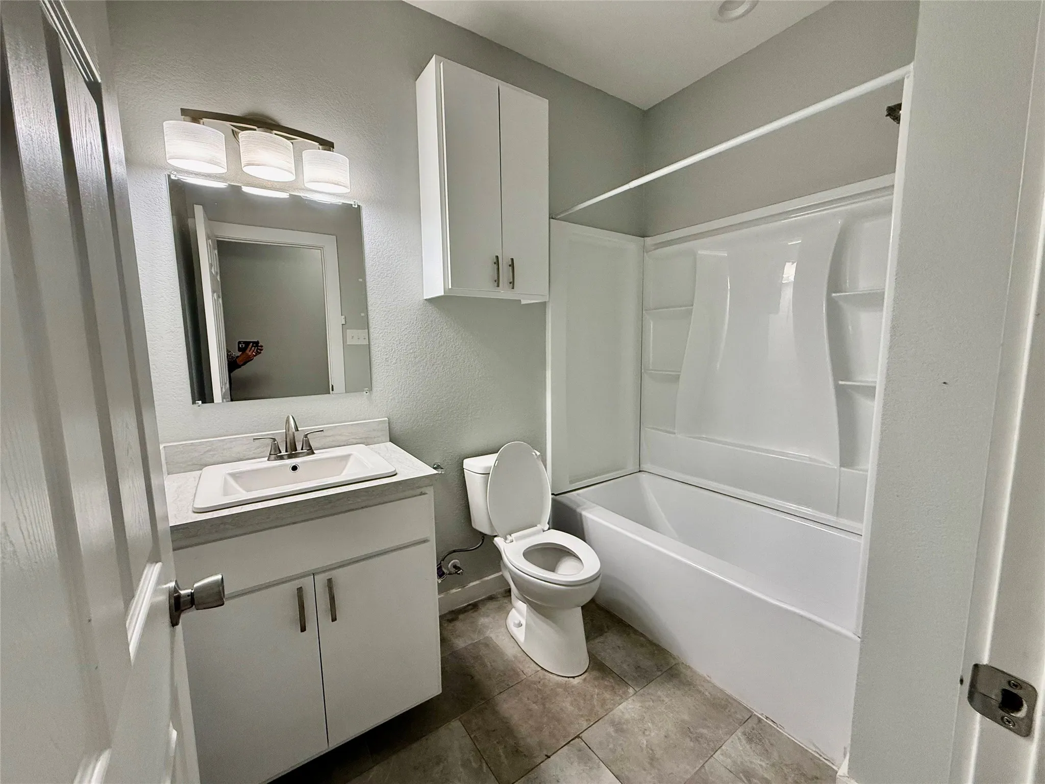 Bathroom featuring a single vanity with a white countertop, coordinating white cabinetry, a built-in bathtub with shower surround, and gray floor tiles