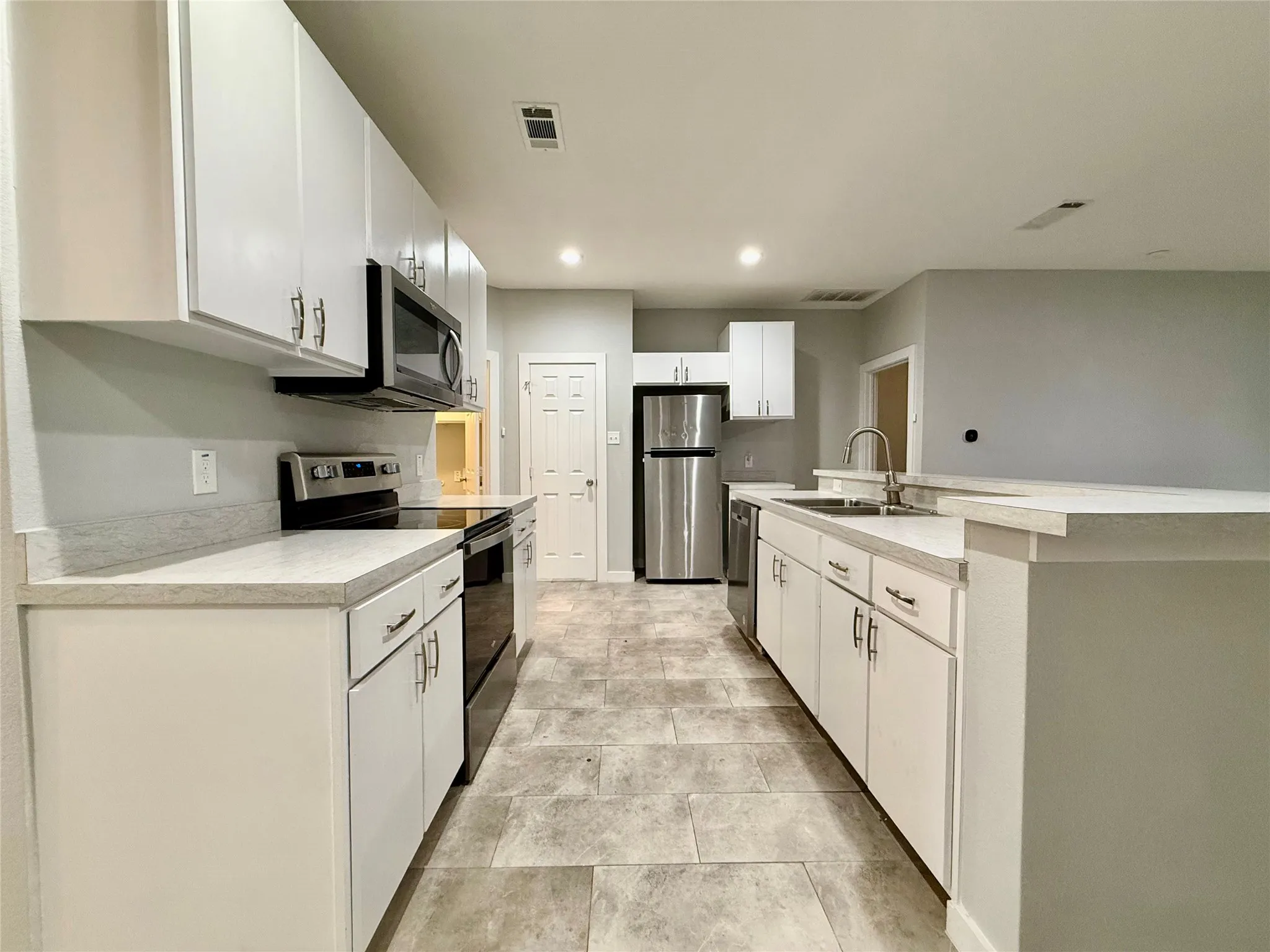 Kitchen featuring white cabinetry, light-toned countertops, stainless steel appliances, and tile flooring