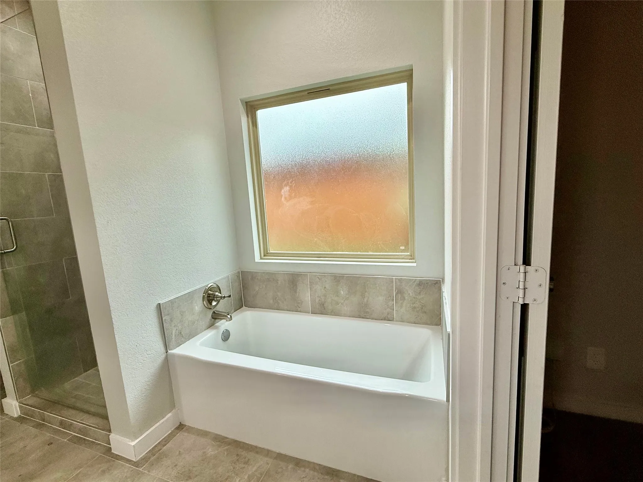 Soaking tub with brushed nickel fixtures, tile surround, and frosted window