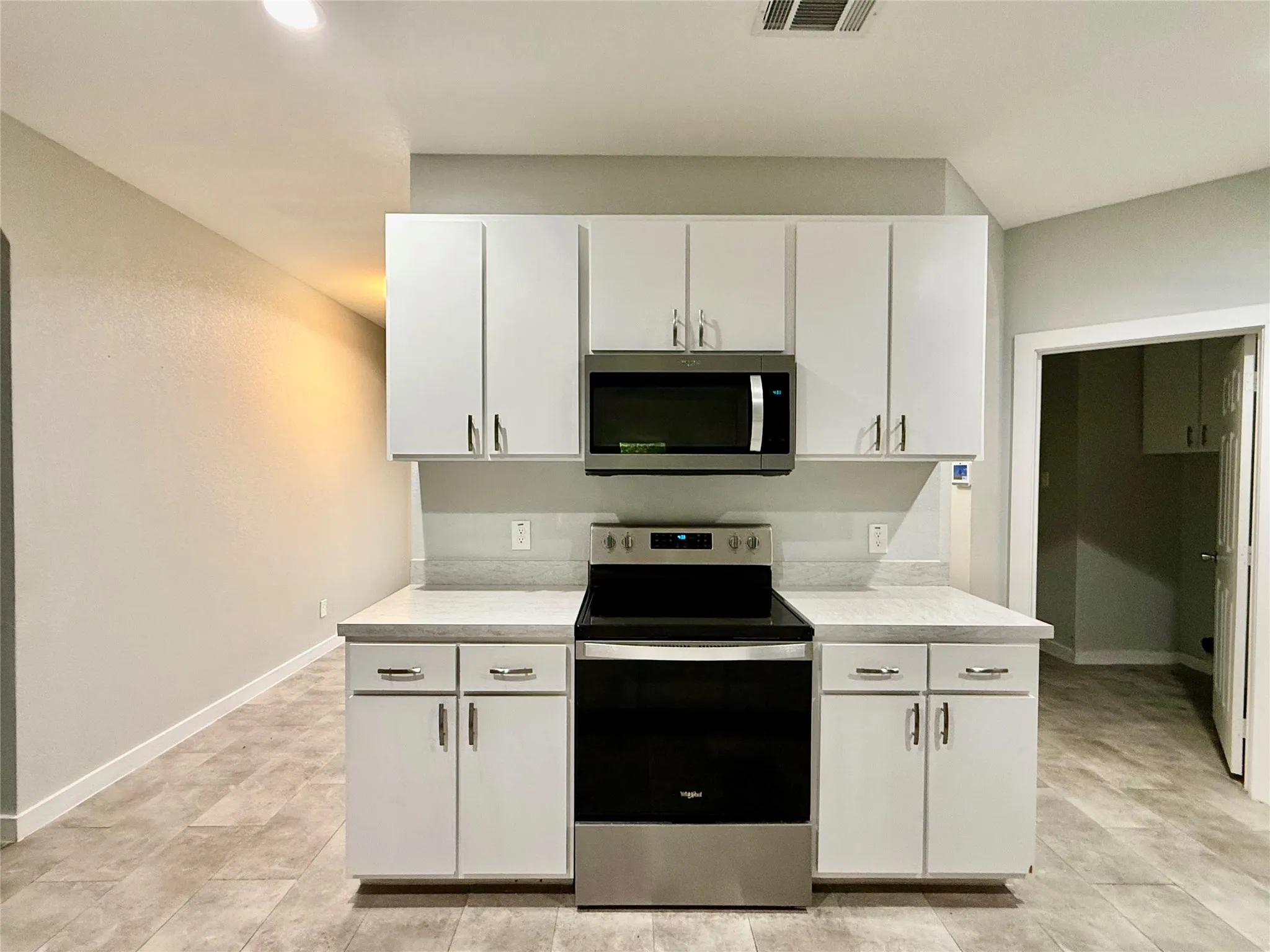 White cabinetry with brushed nickel hardware, stainless steel microwave, stainless steel electric range, light-toned countertops, and wood-finish flooring