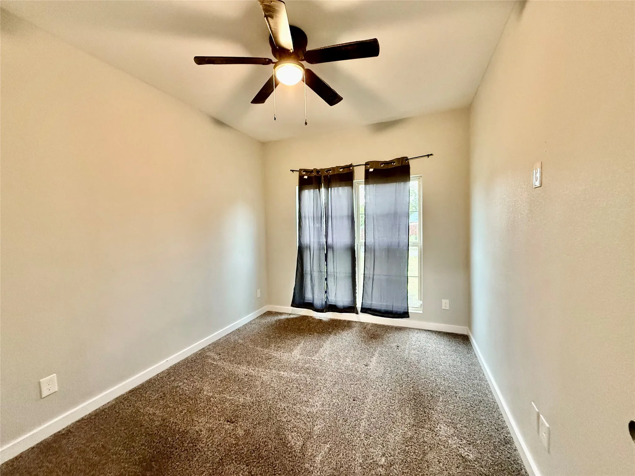Recessed window with dark sheer curtains, textured neutral wall finishes, and ceiling fan with integrated lighting