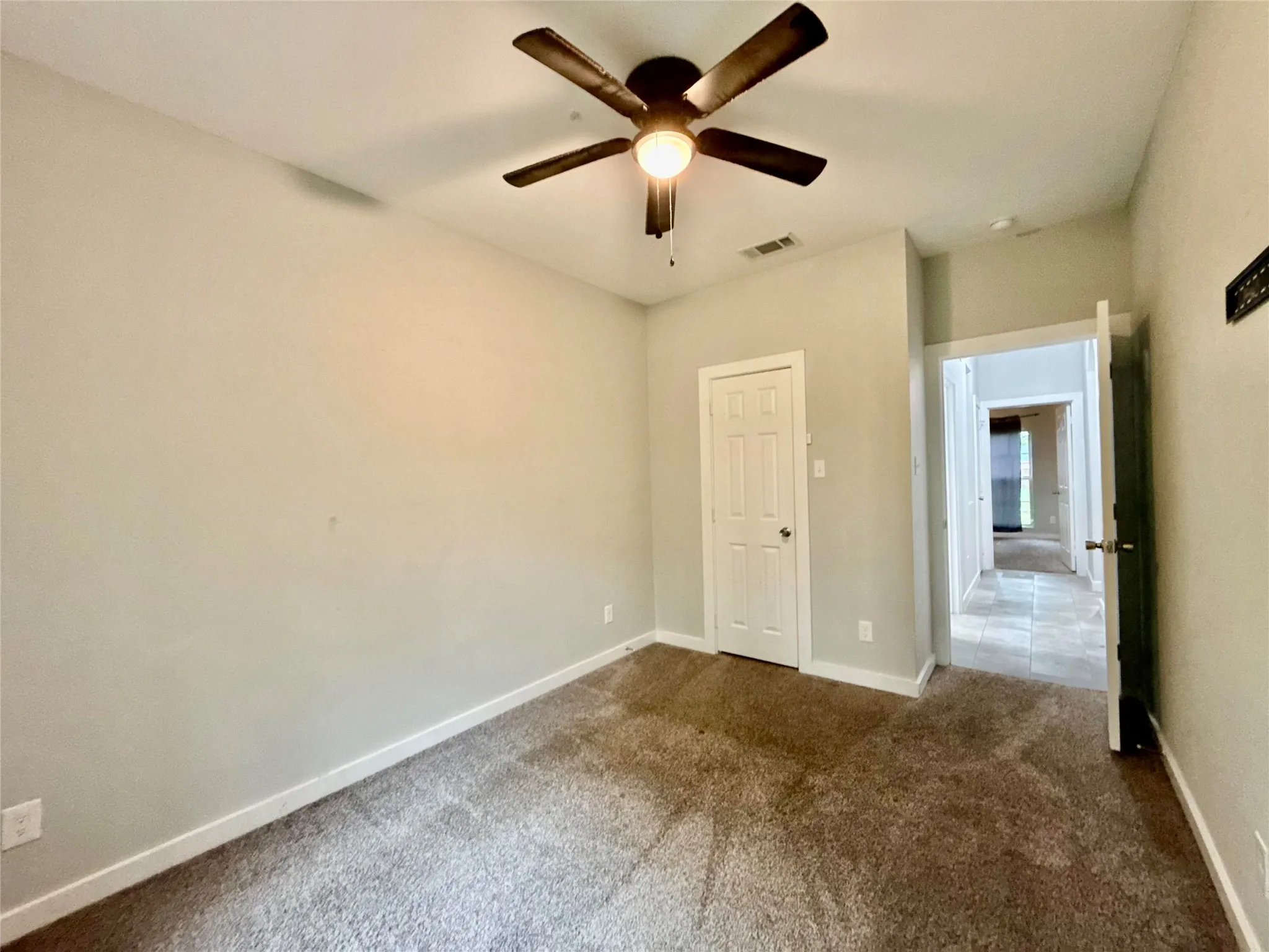 Textured carpeting, neutral wall finish, ceiling fan with integrated lighting, and white paneled door