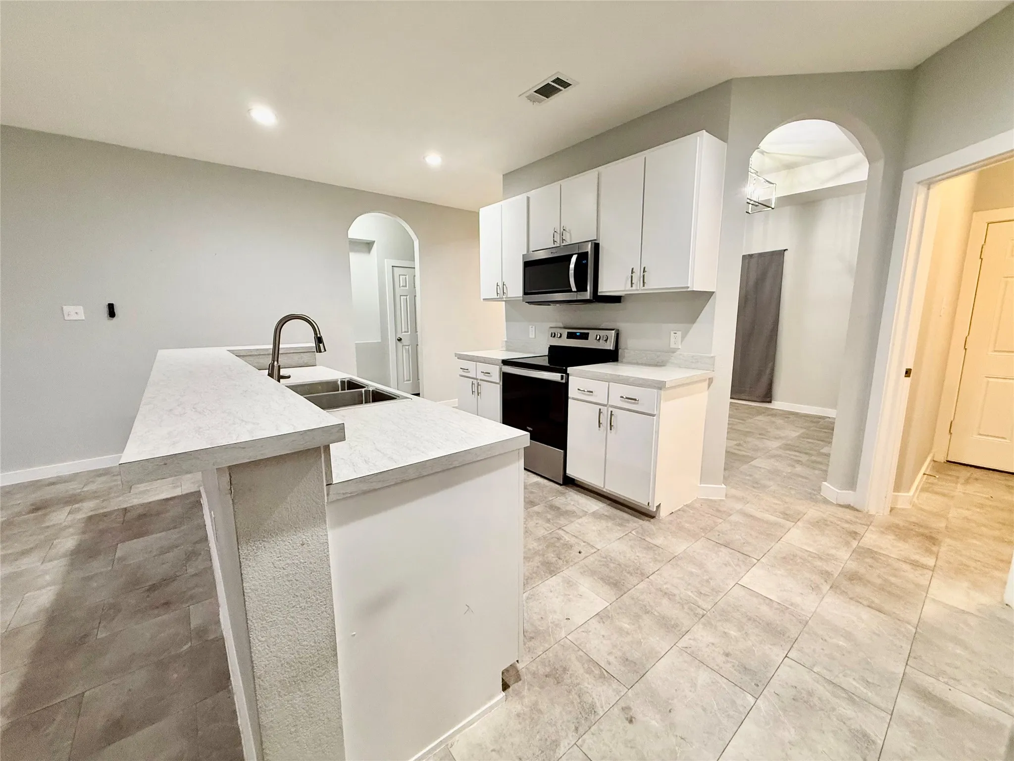 Kitchen featuring a breakfast bar, stainless steel appliances, white cabinetry, a double basin sink with a gooseneck faucet, and tile flooring