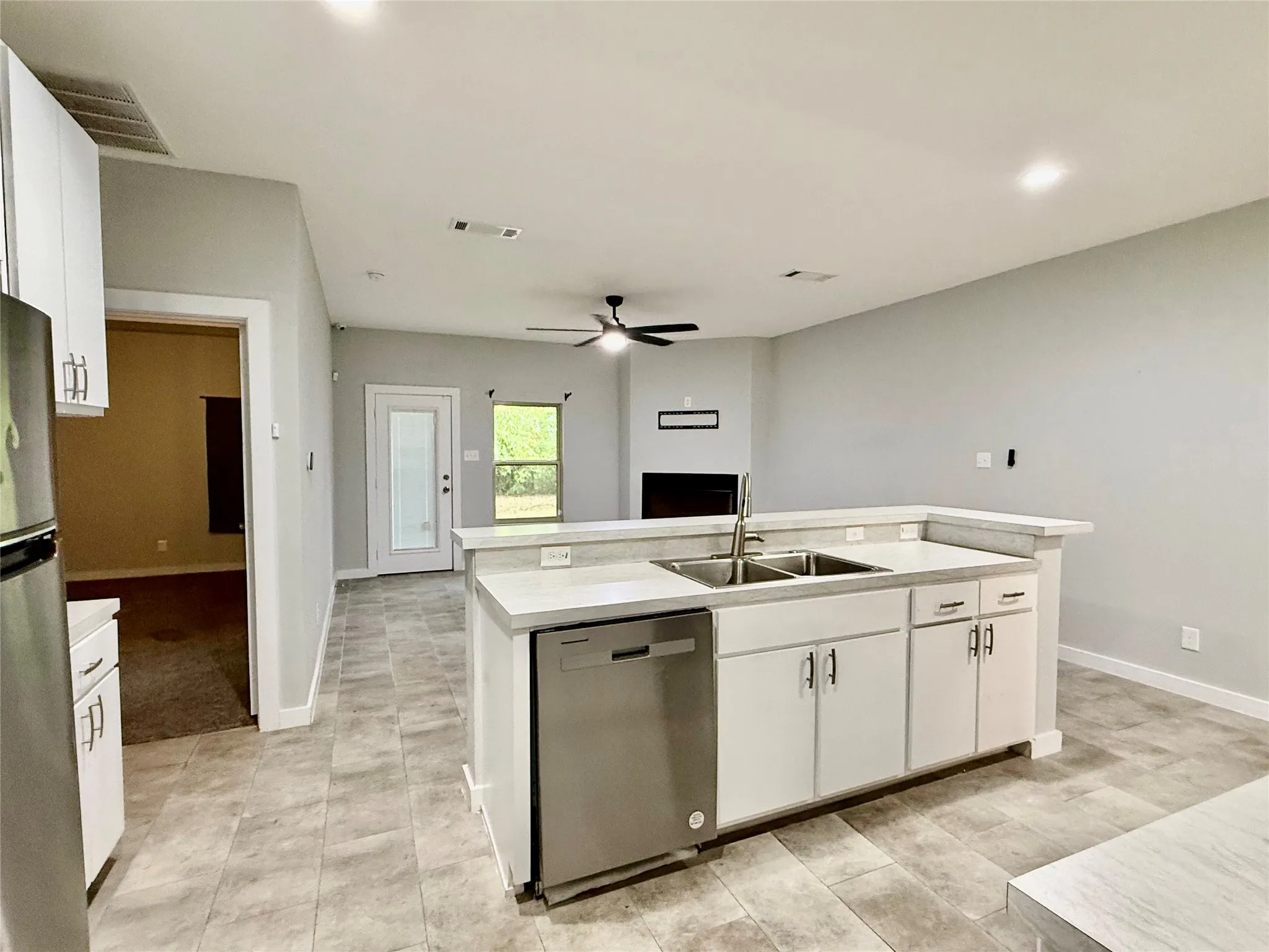 Kitchen island with integrated stainless steel double sink and dishwasher, white cabinetry, and light-toned countertop