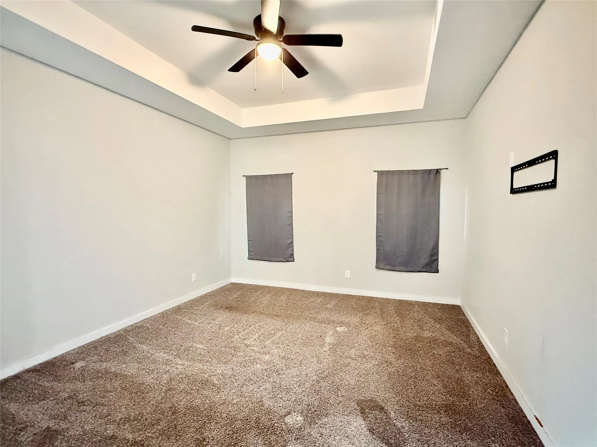 Tray ceiling with a ceiling fan, light neutral wall color, and wall-to-wall carpeting
