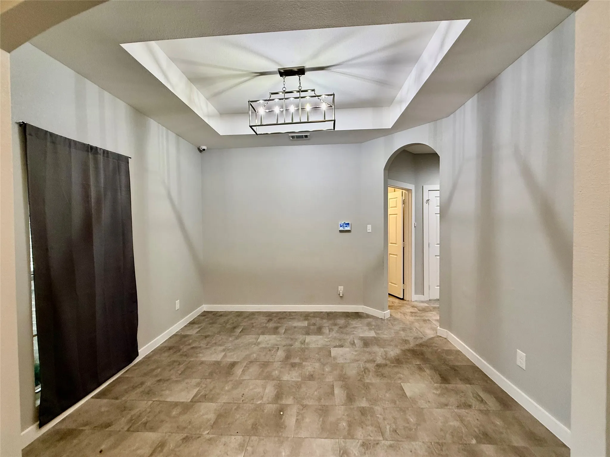 Recessed tray ceiling with a modern rectangular chandelier, neutral wall paint, and tiled flooring