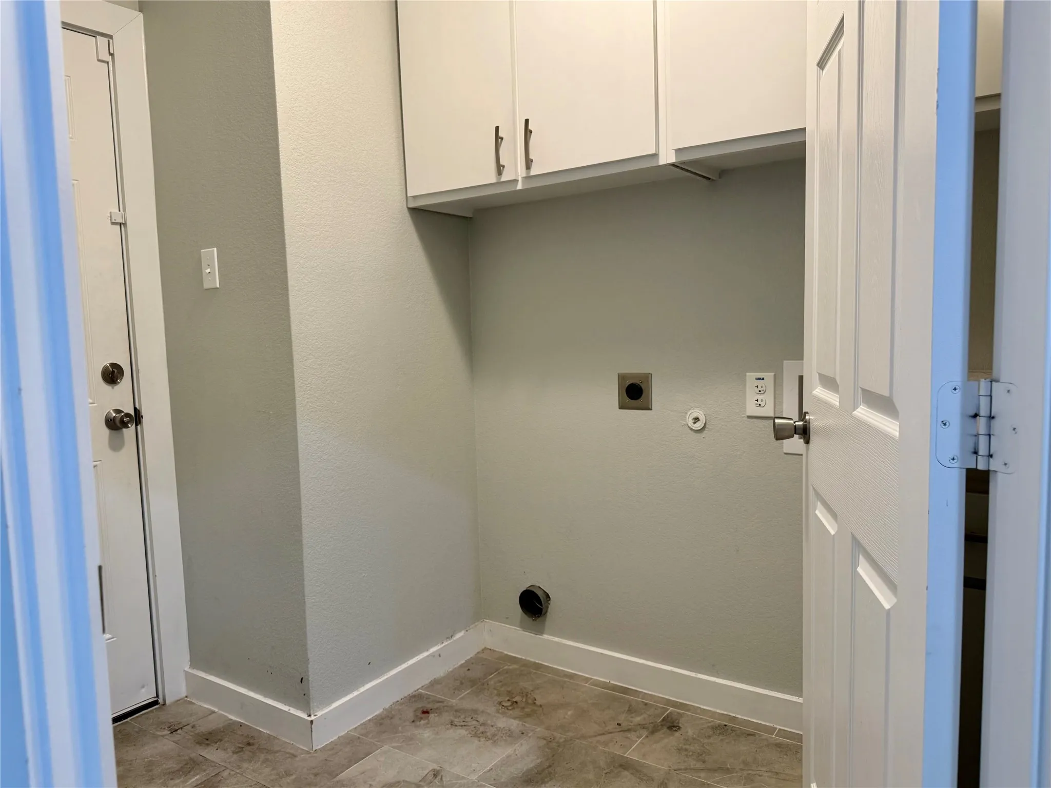 Utility area featuring upper cabinetry with brushed nickel hardware, light neutral wall paint, and tile flooring