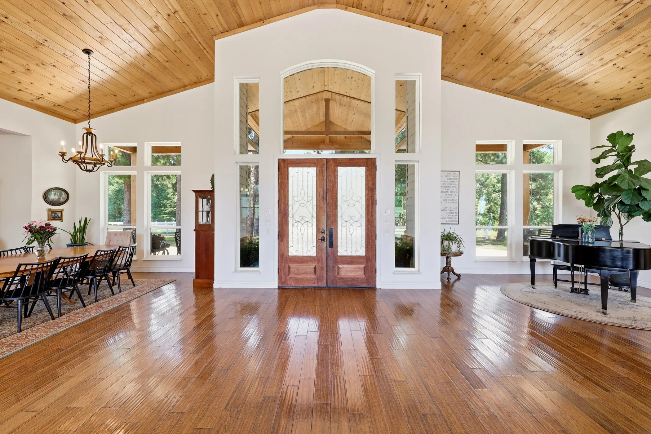 Vaulted wood-paneled ceiling, wood-finish flooring, double entry doors with decorative glass, tall windows, and a chandelier