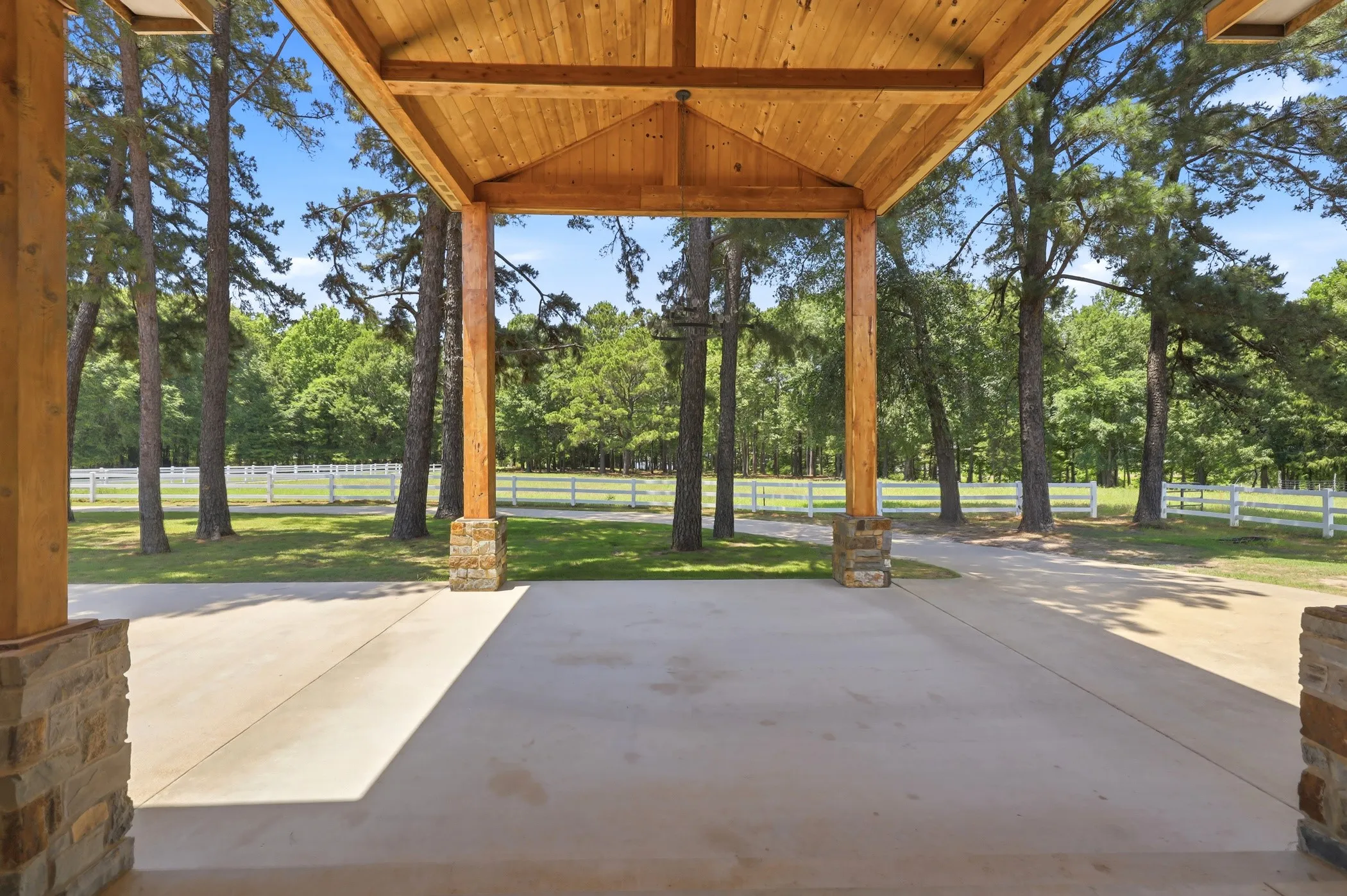 Covered portico with a wood-plank ceiling, exposed wood beams, and stone-clad columns