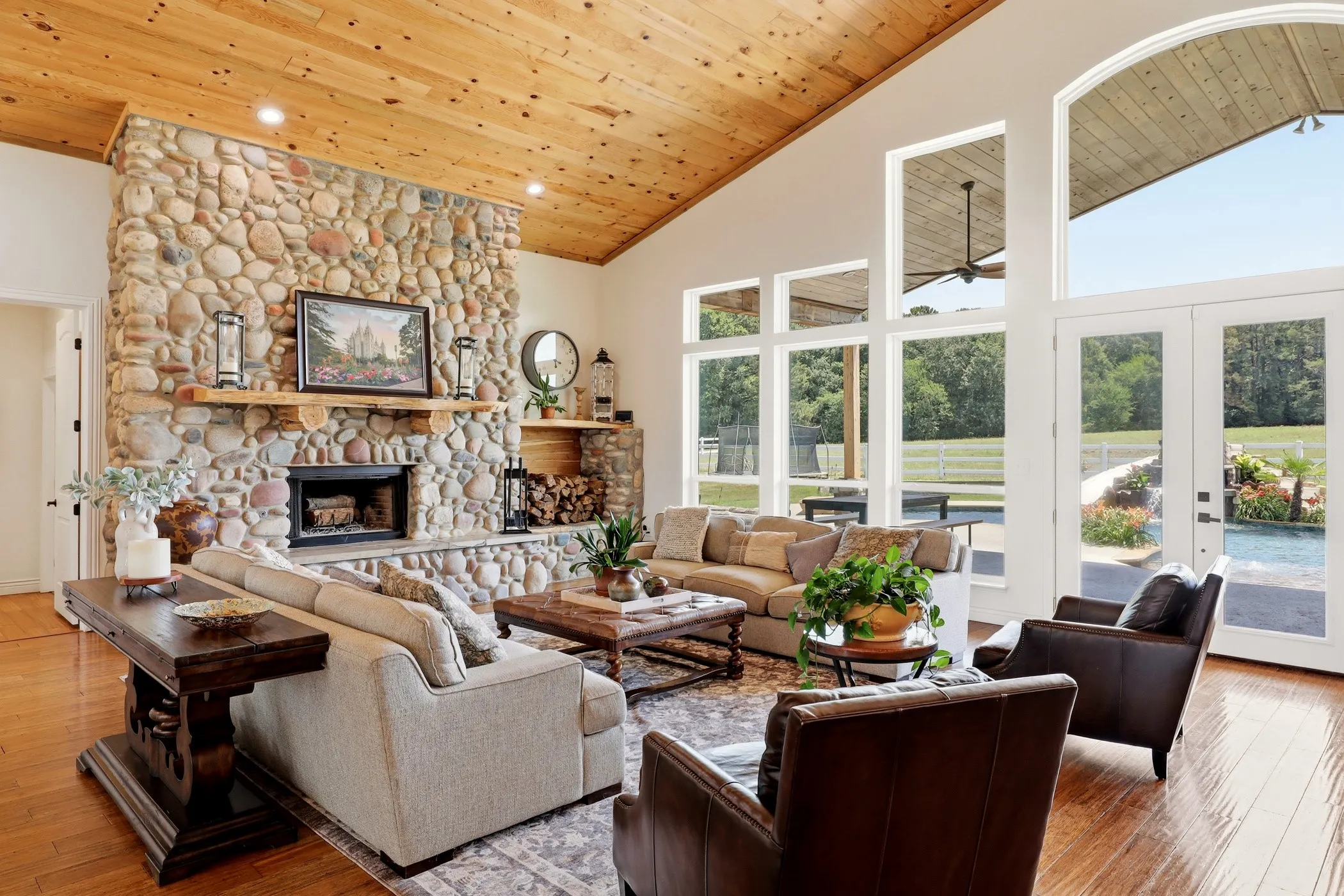 Vaulted wood-paneled ceiling, floor-to-ceiling stone fireplace, wood-finish flooring, and multiple glass doors with transom windows