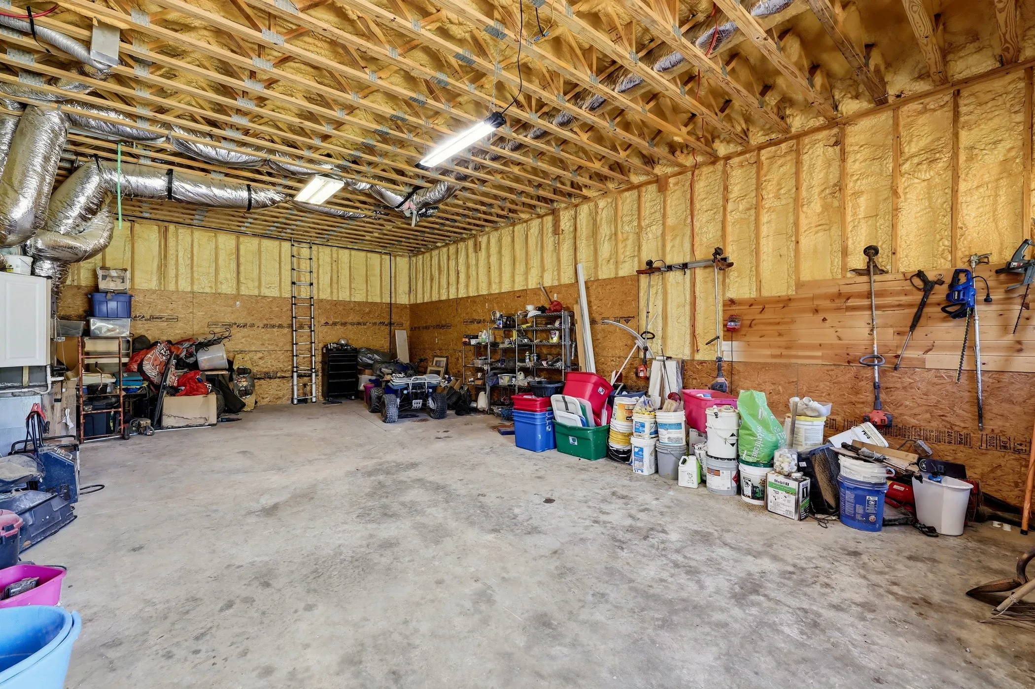 Spacious utility room featuring a concrete floor, exposed wood ceiling trusses, and insulated walls
