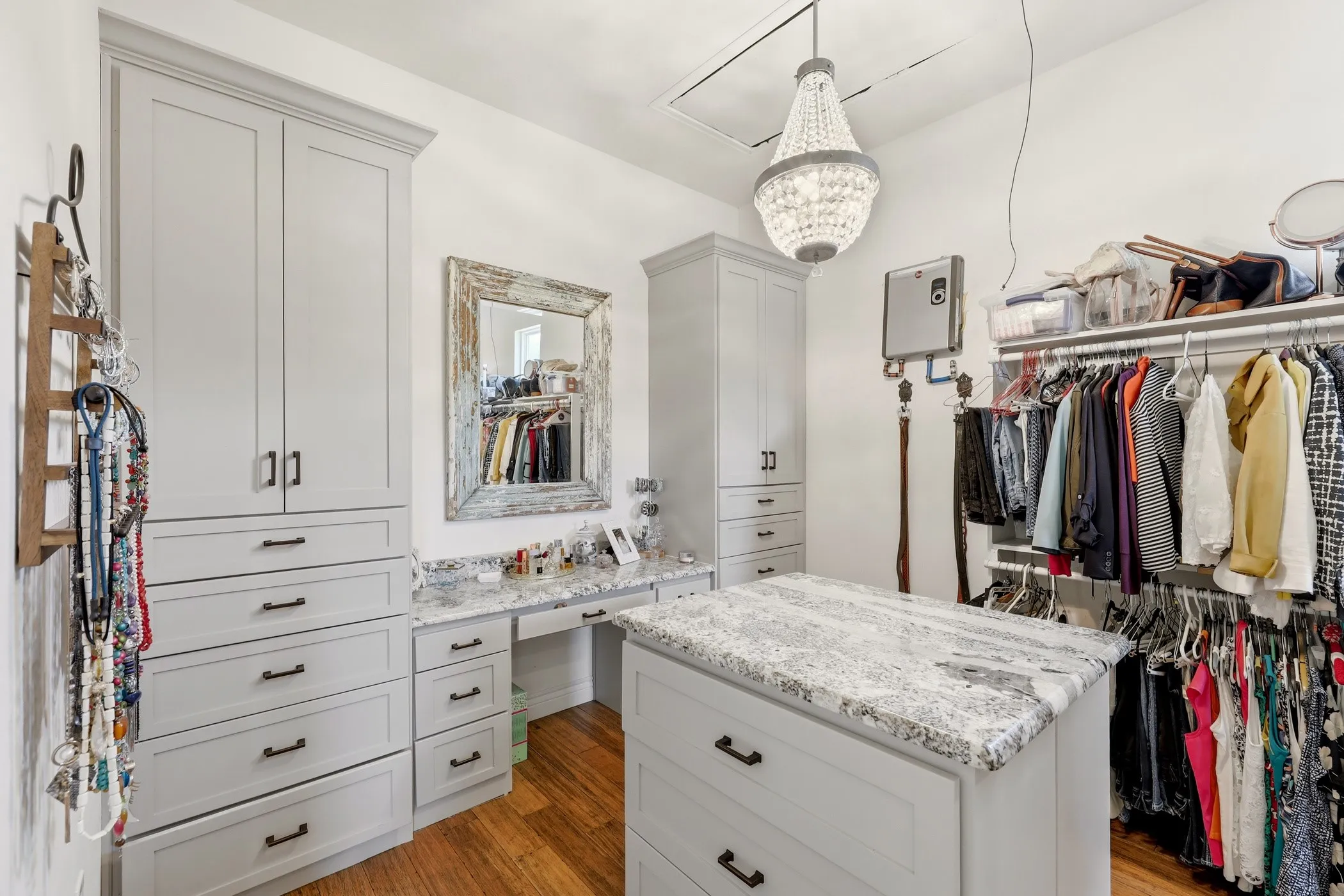 Custom cabinetry with integrated drawers, spacious built-in shelving, center island with stone countertop, wood-finish flooring, and a crystal chandelier