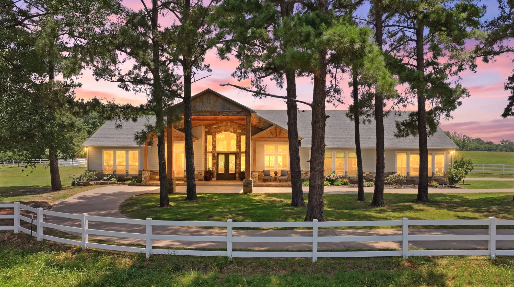 Expansive property featuring a white fence, mature trees, a circular driveway, and a covered porch entry