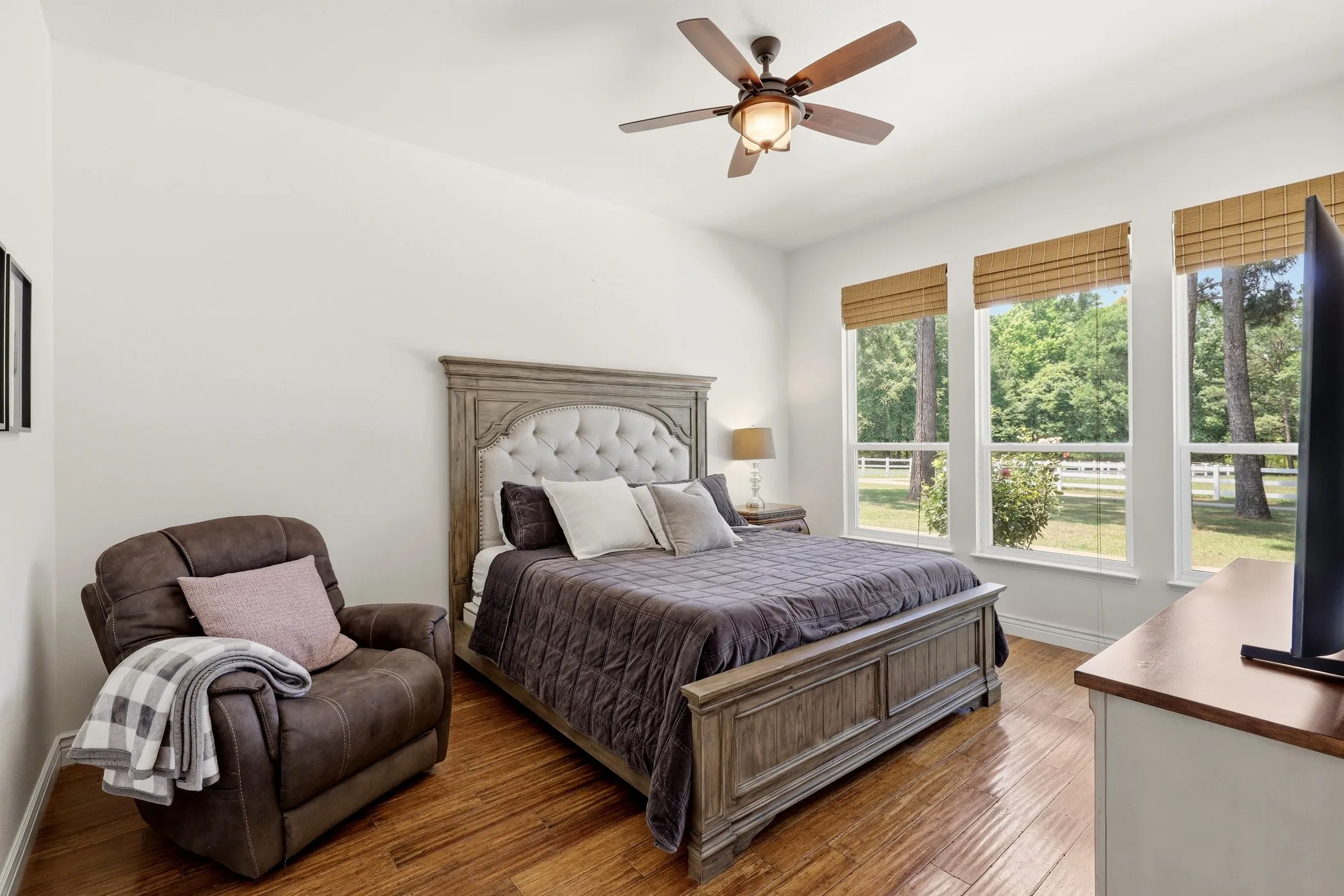 Hardwood flooring, three large windows, ceiling fan with integrated lighting, and white walls