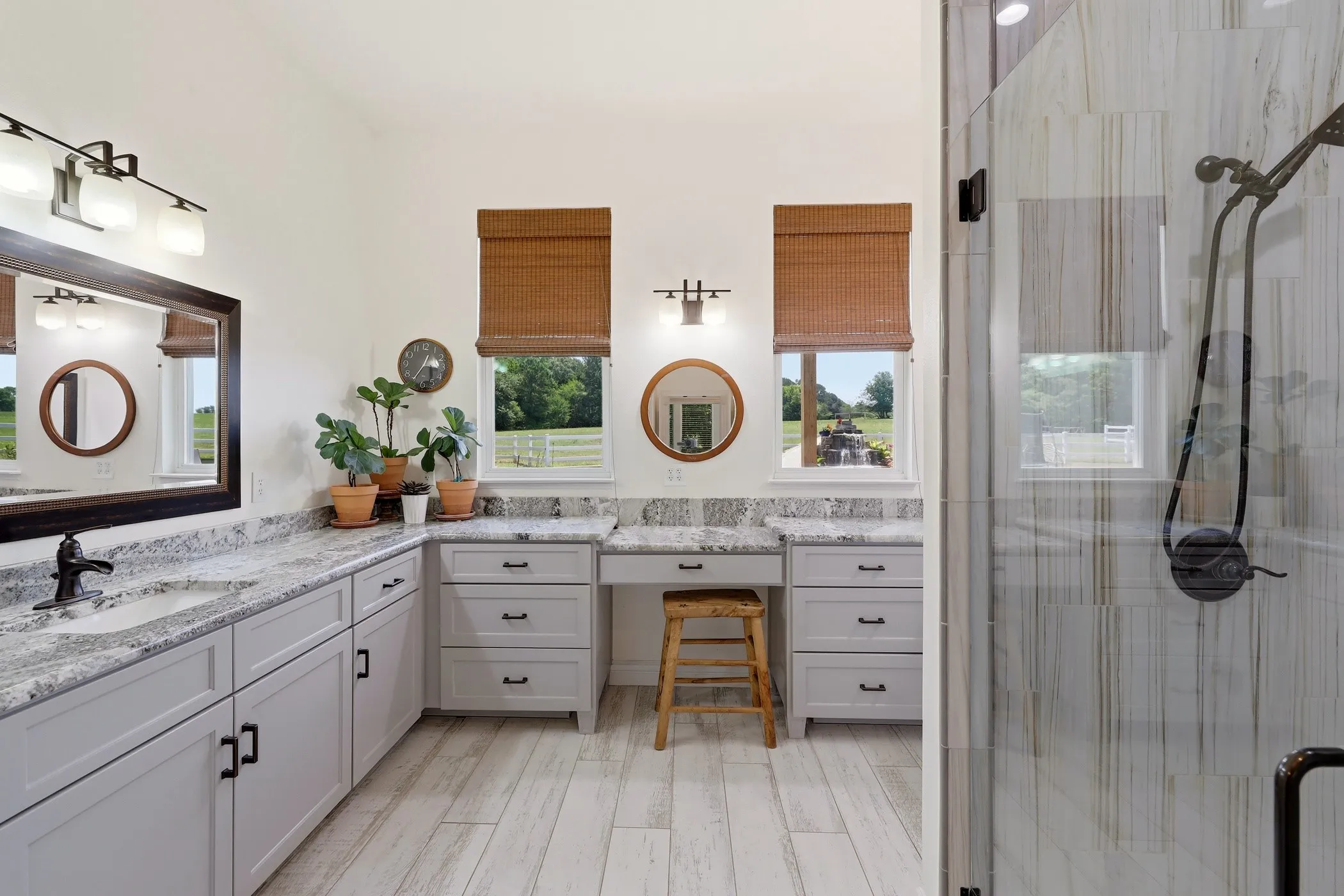 Dual vanity with stone countertops, built-in cabinetry, wood-finish flooring, and a glass-enclosed shower
