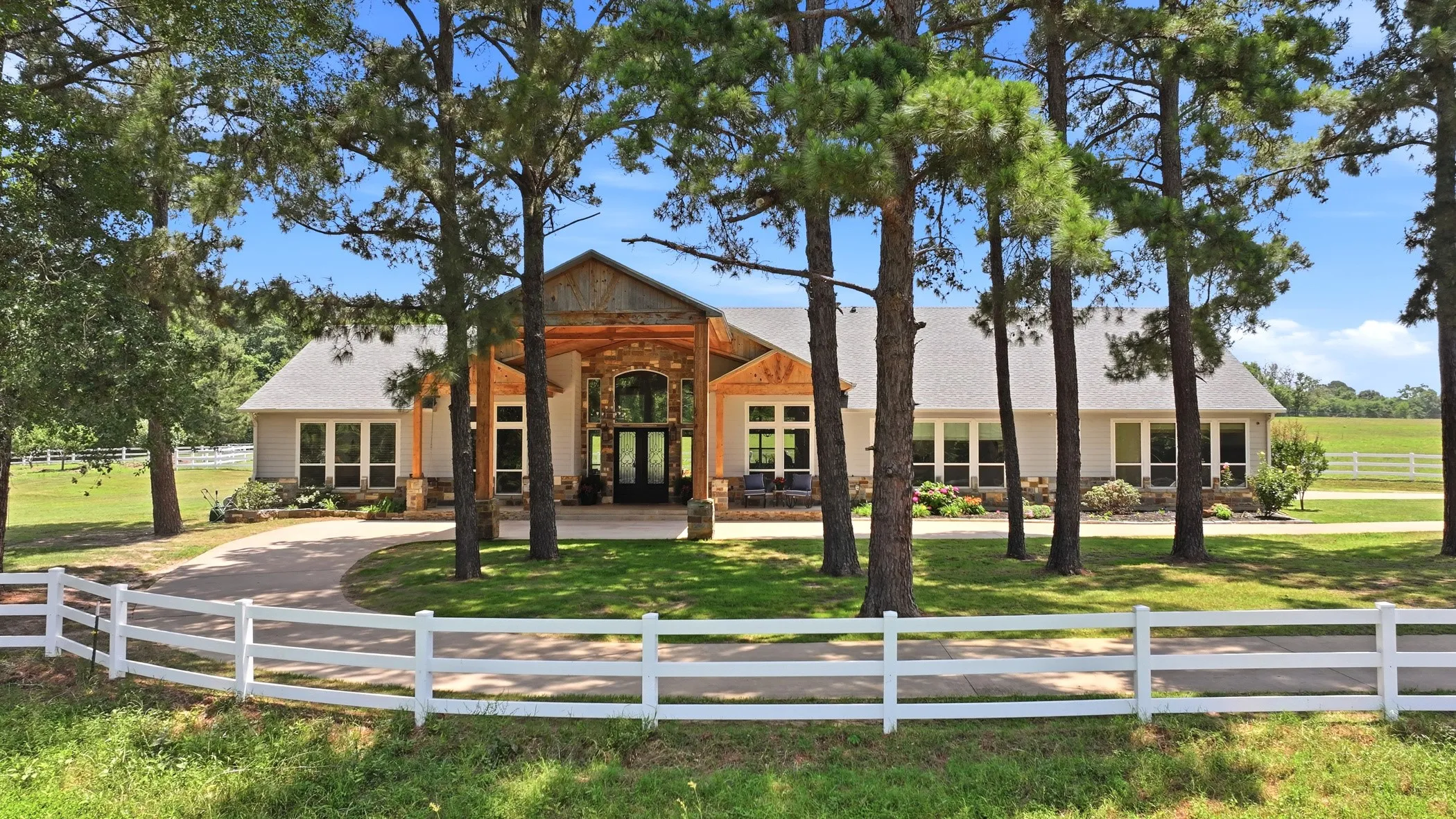 Ranch-style residence featuring a stone and wood beam portico, a curved driveway, and a white picket fence