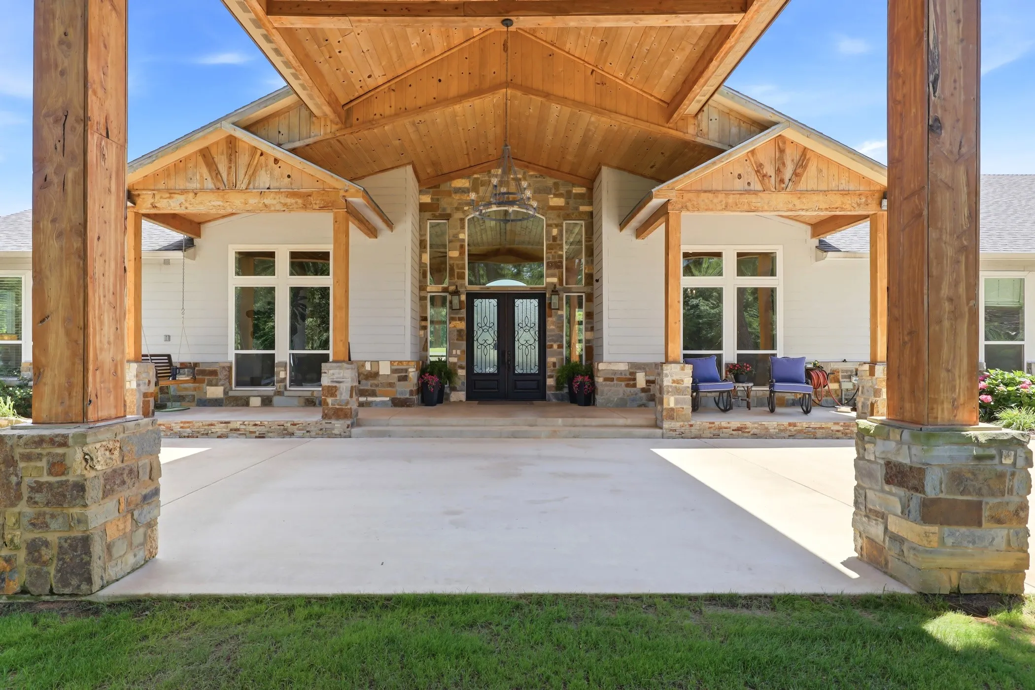 Covered entry with exposed wood ceiling, stone columns, and double front doors