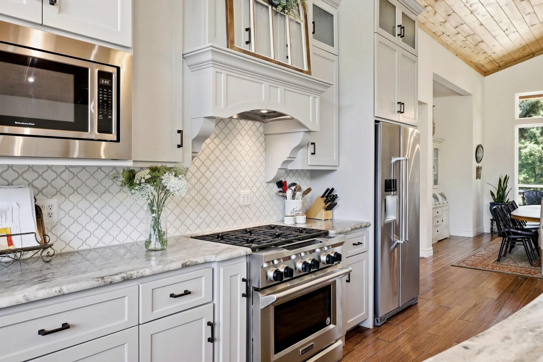 Gourmet kitchen with stainless steel appliances, custom cabinetry, stone countertops, decorative tile backsplash, and wood-finish flooring
