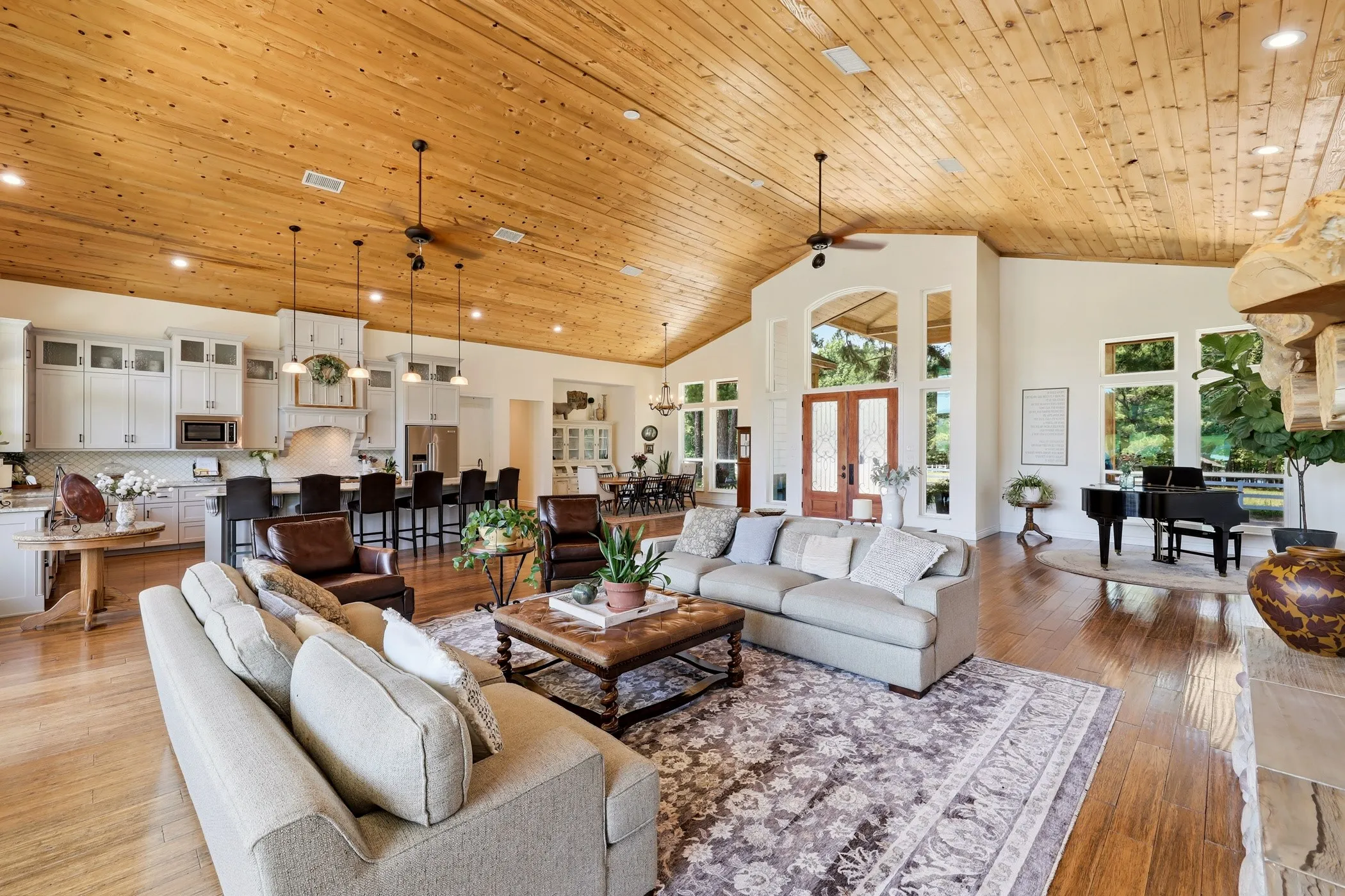 Vaulted wood-finish ceiling, wood-finish flooring, white cabinetry, a large kitchen island with seating, and ample natural light from multiple windows