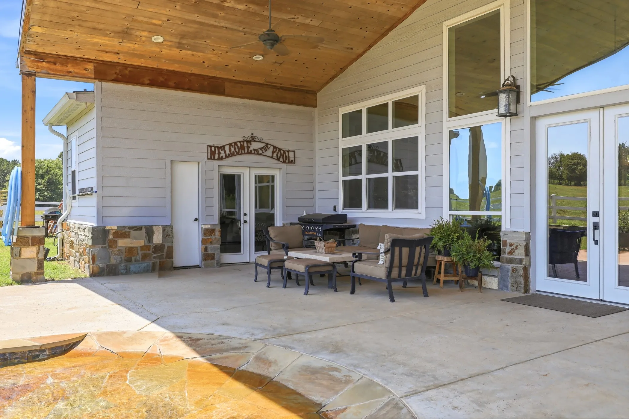 Expansive covered patio featuring a wood-finish ceiling, stone accents, multiple large windows, and a ceiling fan