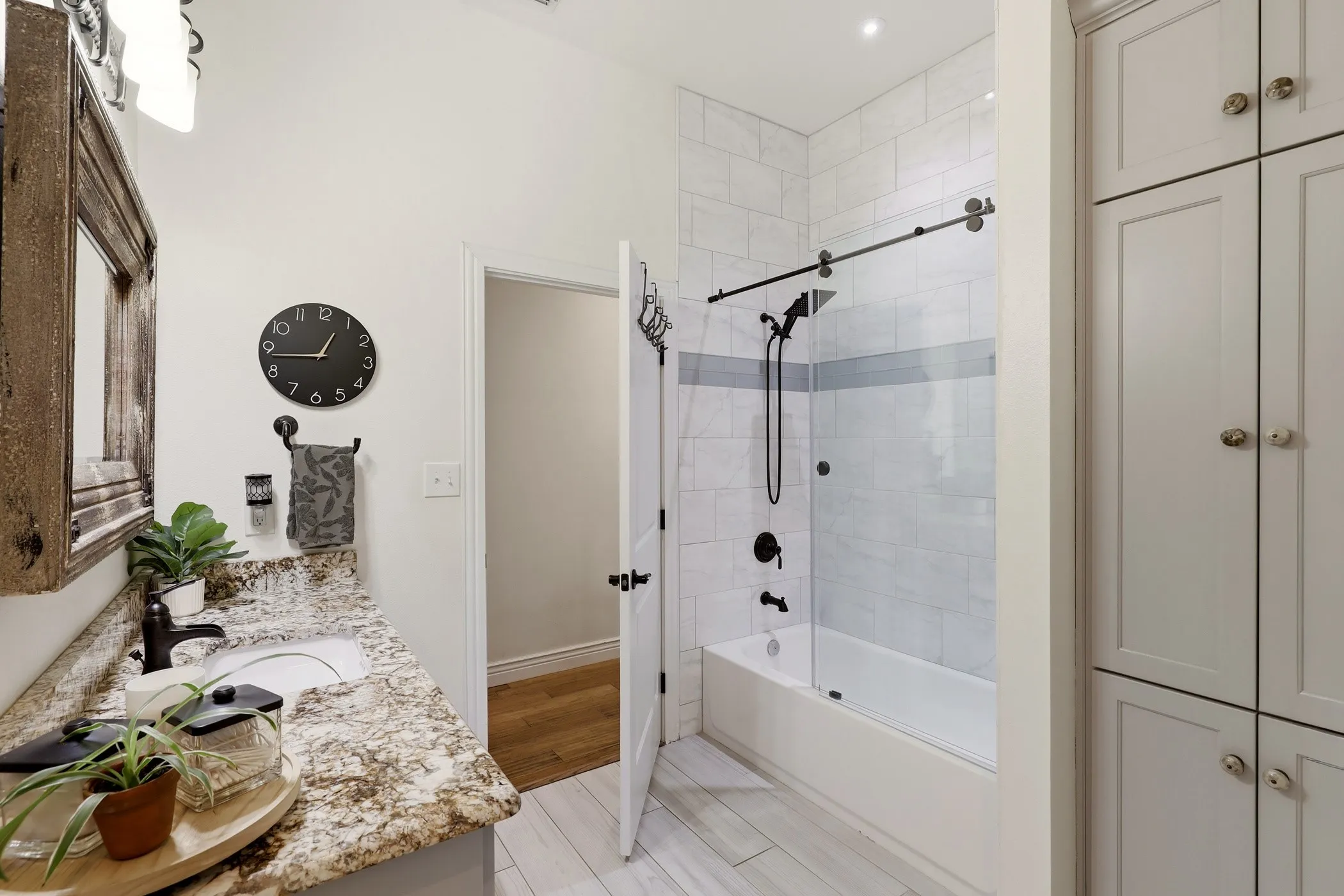 Bathroom featuring a tub/shower combination with sliding glass door, white subway tile surround, matte black fixtures, a single vanity with granite countertop, and built-in cabinetry