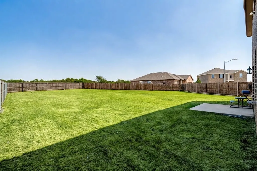 Expansive backyard featuring a manicured lawn, wood privacy fencing, and a concrete patio