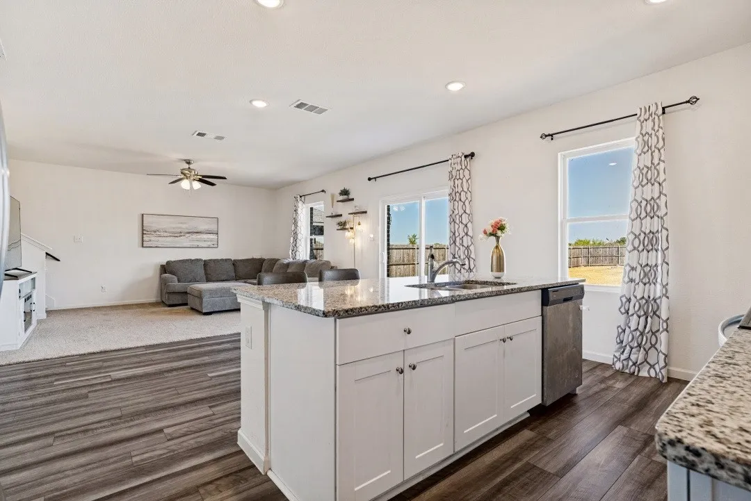 Kitchen island with a stainless steel sink, white cabinetry, and granite countertops
