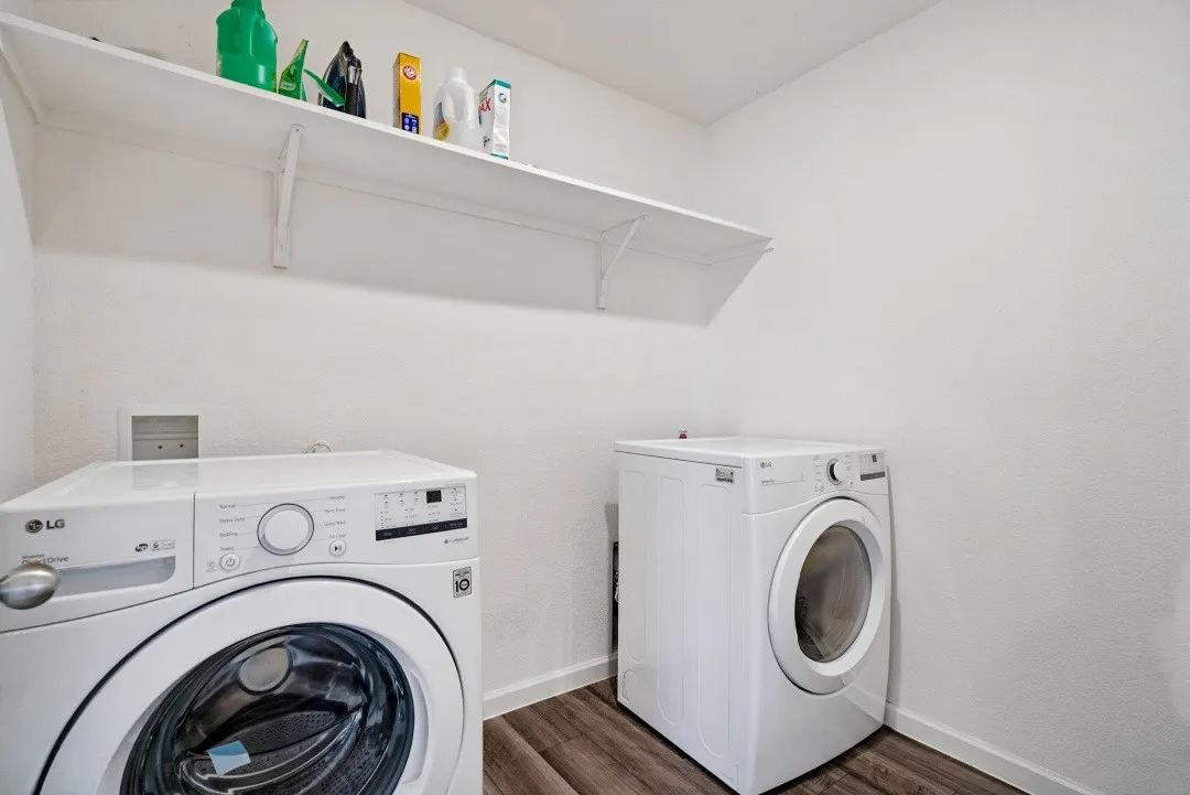 Laundry area with wood-finish flooring and a wall-mounted storage shelf
